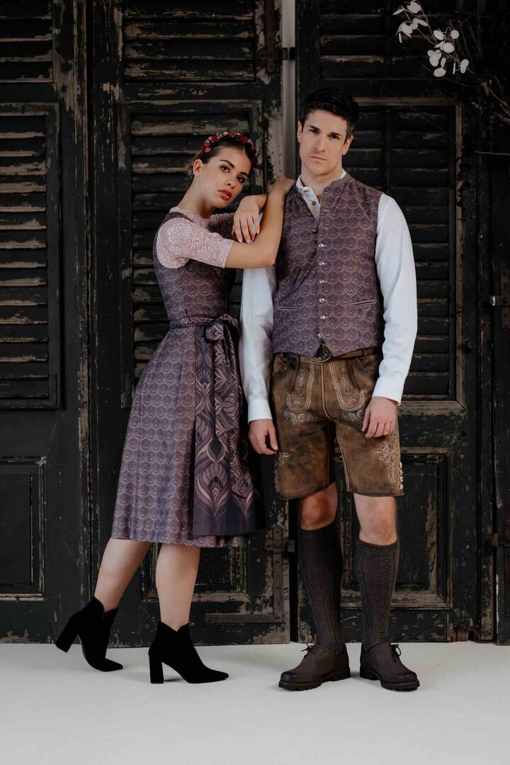 Frau im lila-gemustertem Dirndl lehnt sich an Mann mit zum Dirndl passender Weste