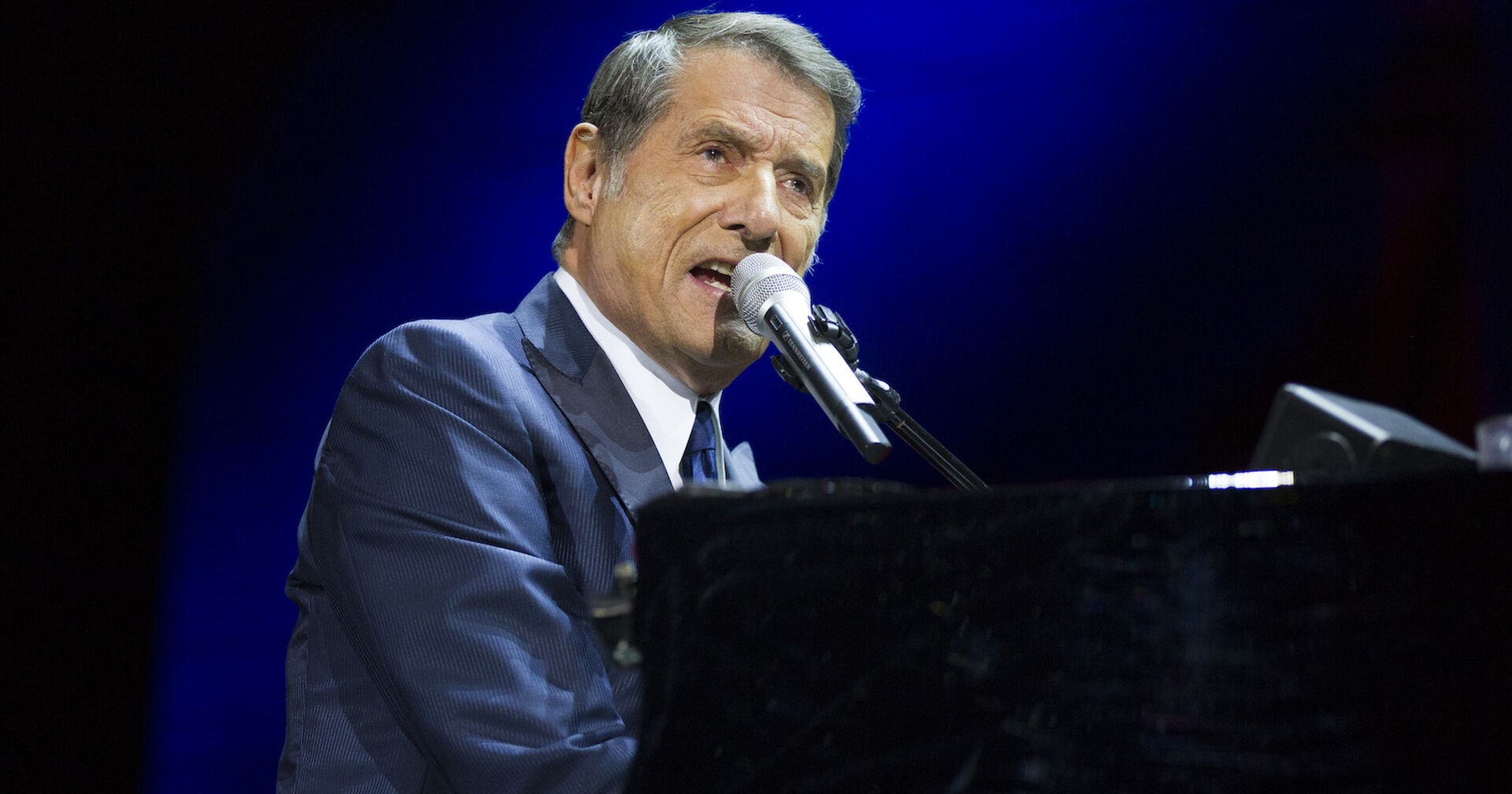Udo Jürgens singt auf einer Bühne und spielt dabei auf einem Klavier.