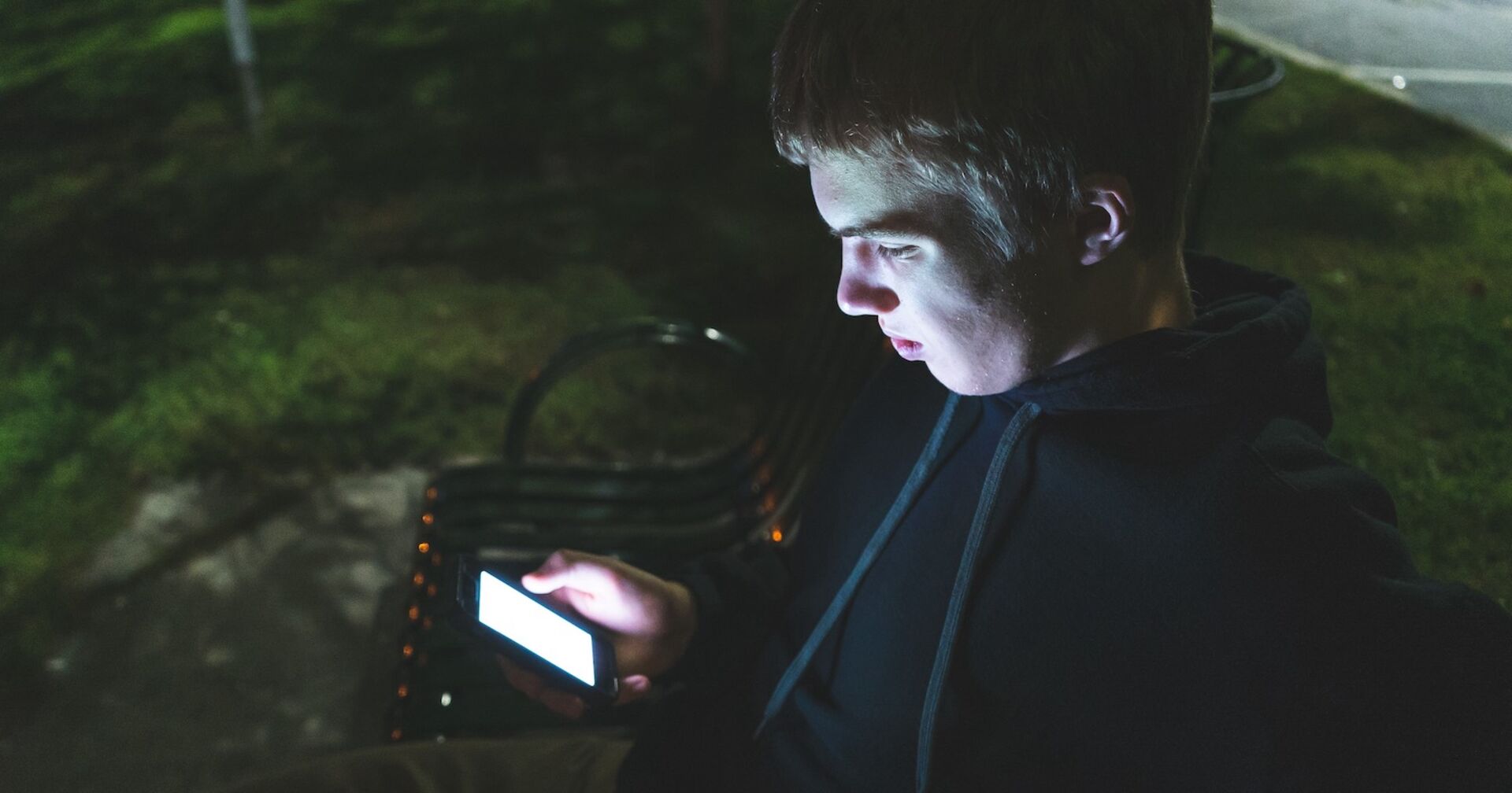 Ein Jugendlicher steht im Dunkeln und starrt auf sein Handy.