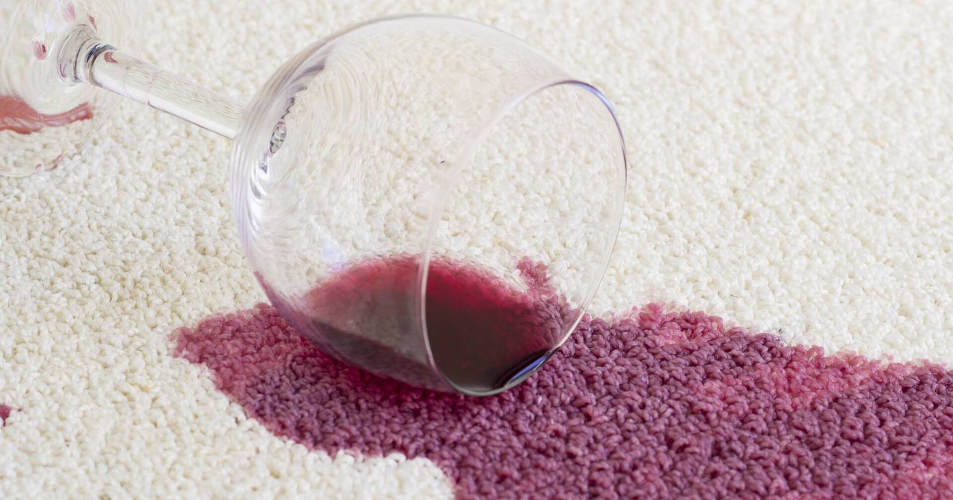 Verschüttetes Glas mit Rotwein auf weißen Teppich