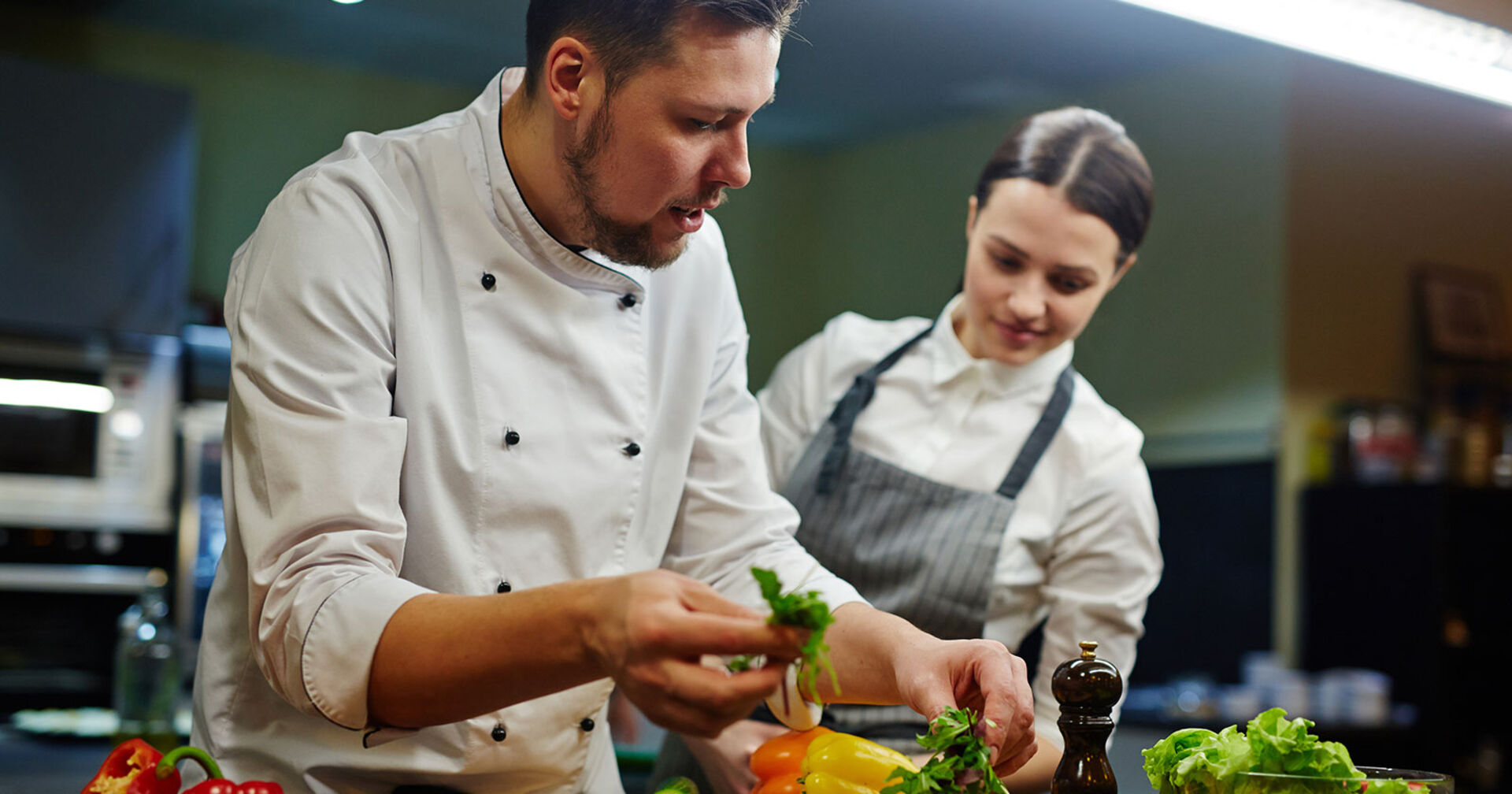 Koch bringt einem weiblichen Lehrling bei, wie man ein Gericht appetitlich anrichtet | Credit: iStock.com/shironosov
