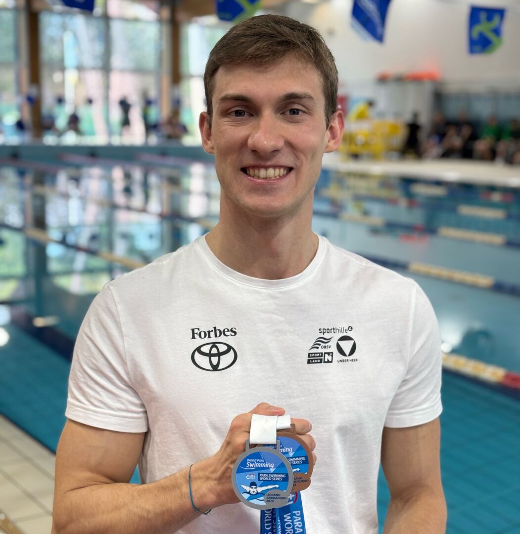 Porträt vor Schwimmbecken mit Medaillen in der Hand