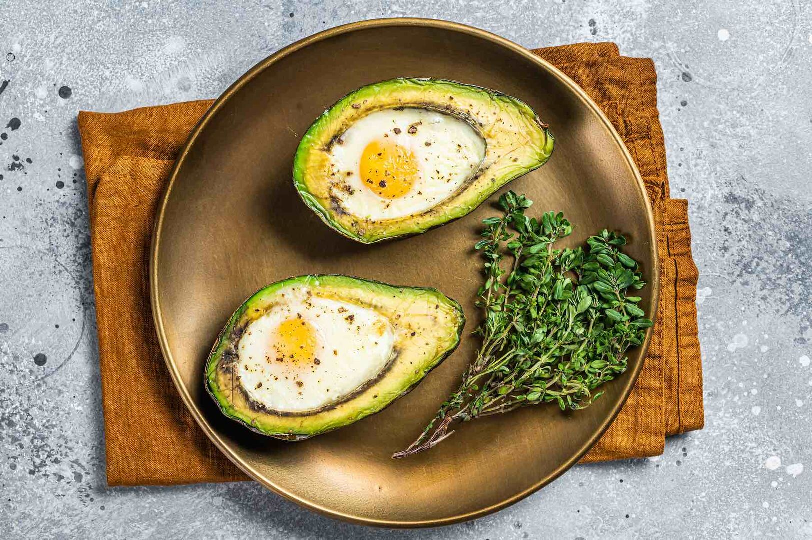 Eine mit Spiegelei gefüllte Avocado auf einem Teller angerichtet.