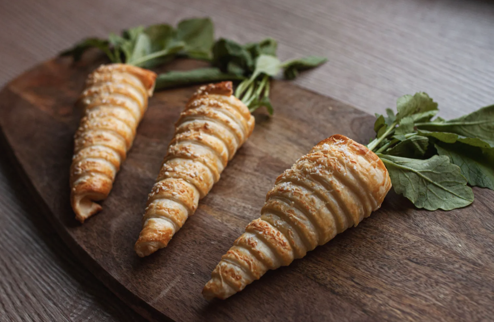 Drei Blaetterteigkarotten auf einem Holzbrett dekoriert.