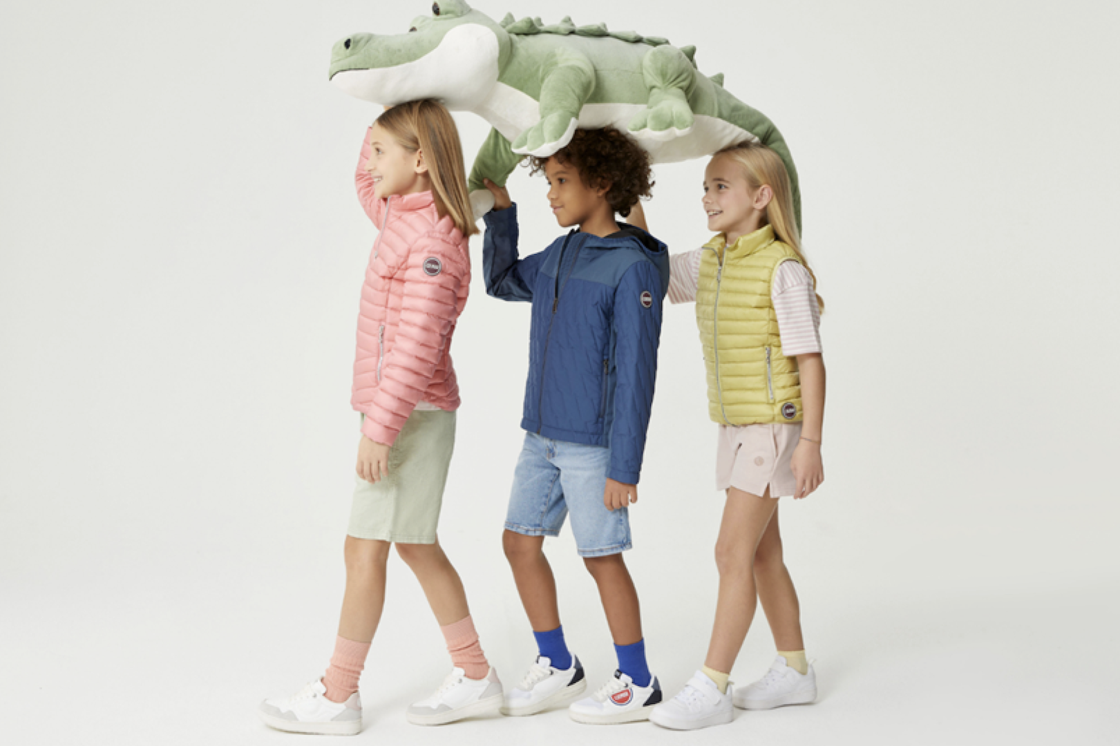 Drei Kinder in bunten Jacken mit Stofftier