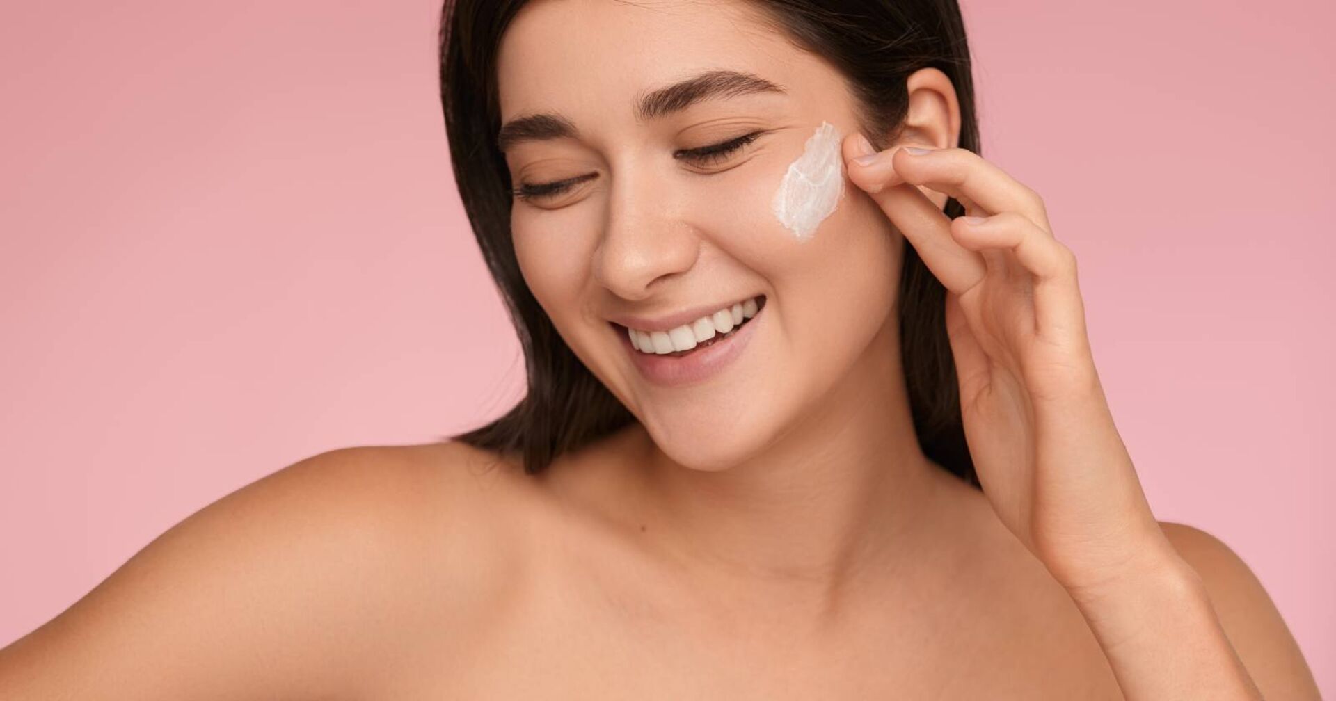 Nahaufnahme des Gesichts einer jungen Frau, die einen Cremetupfer auf der Wange hat und lächelt.