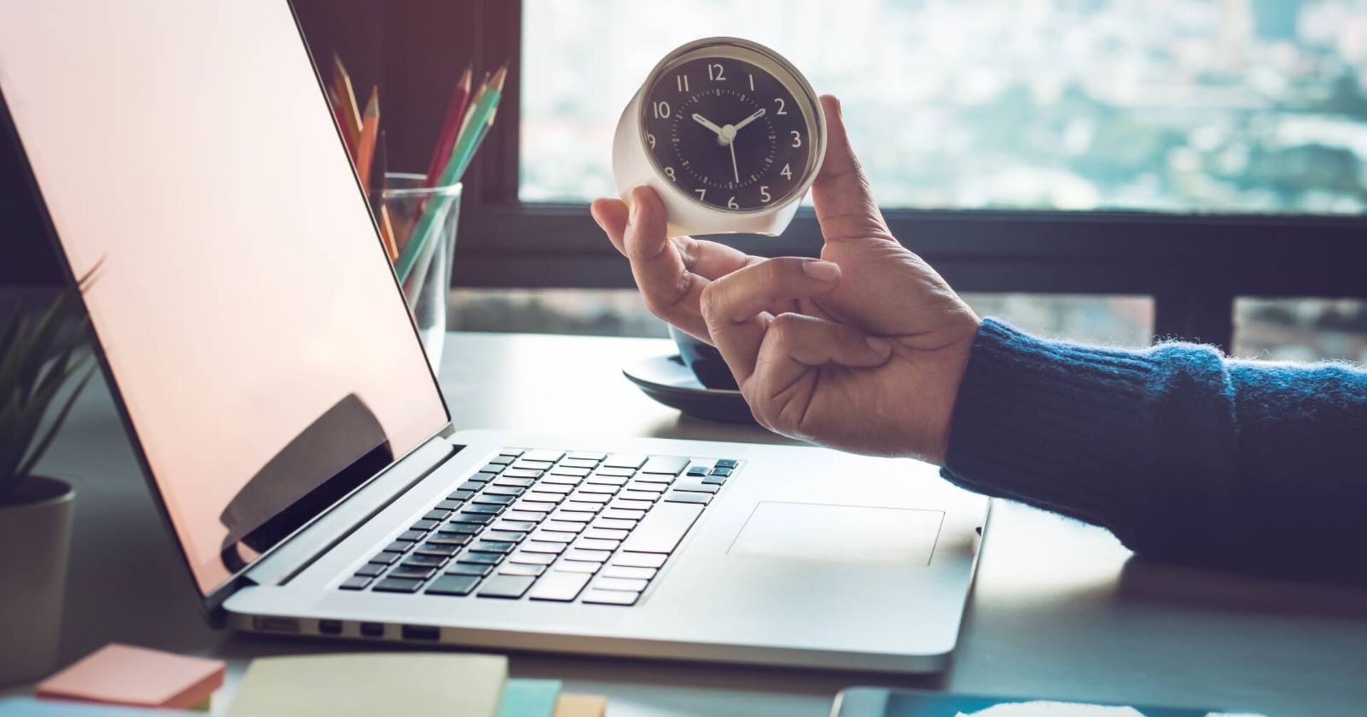 Schreibtisch mit Laptop, Uhr und Stifteköcher