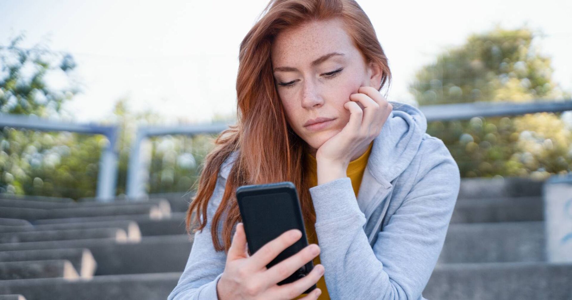 Junge Frau, die traurig auf das Display ihres Smartphones schaut.