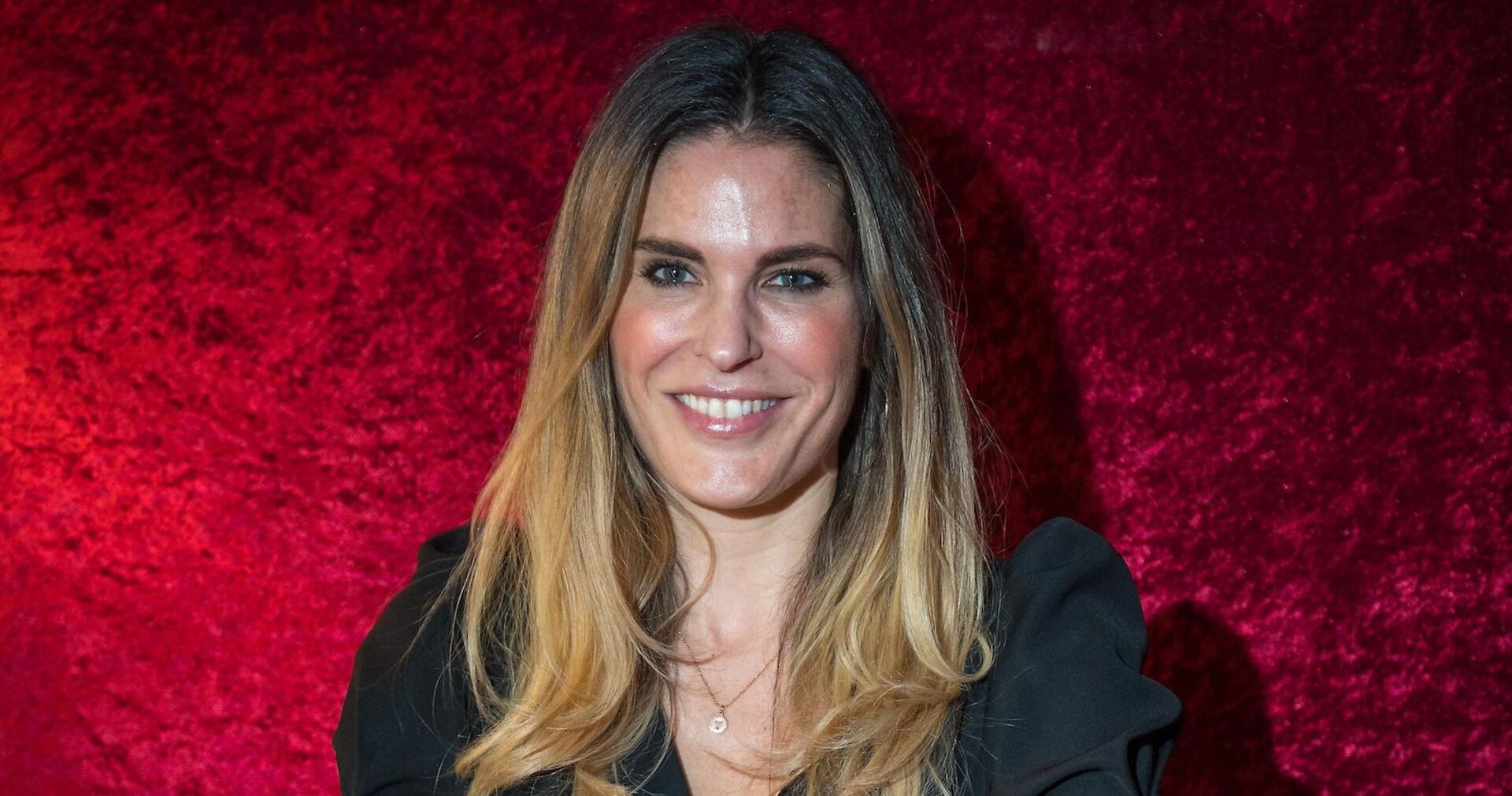 Elke Rock mit offenen blonden Haaren vor einer roten Wand.