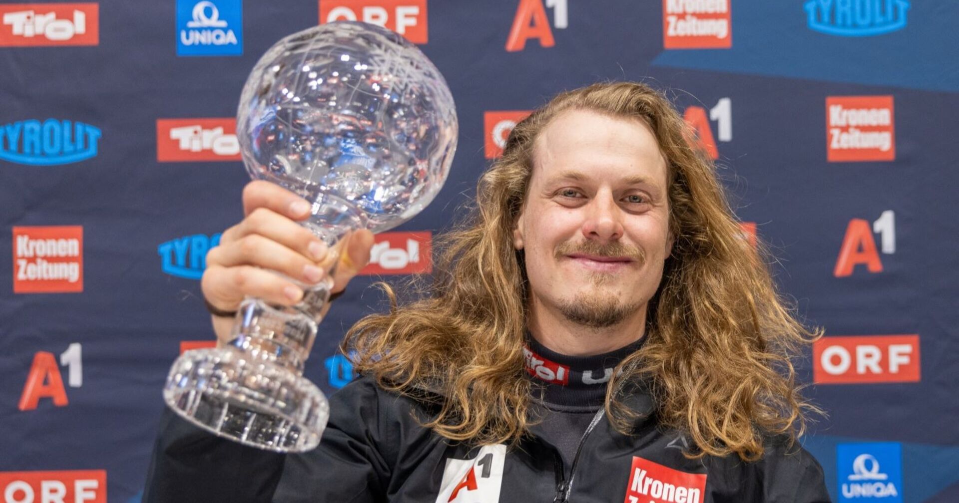 Manuel Feller mit wallender Mähne und seine Weltcup-Kugel bei einem offiziellen Fototermin