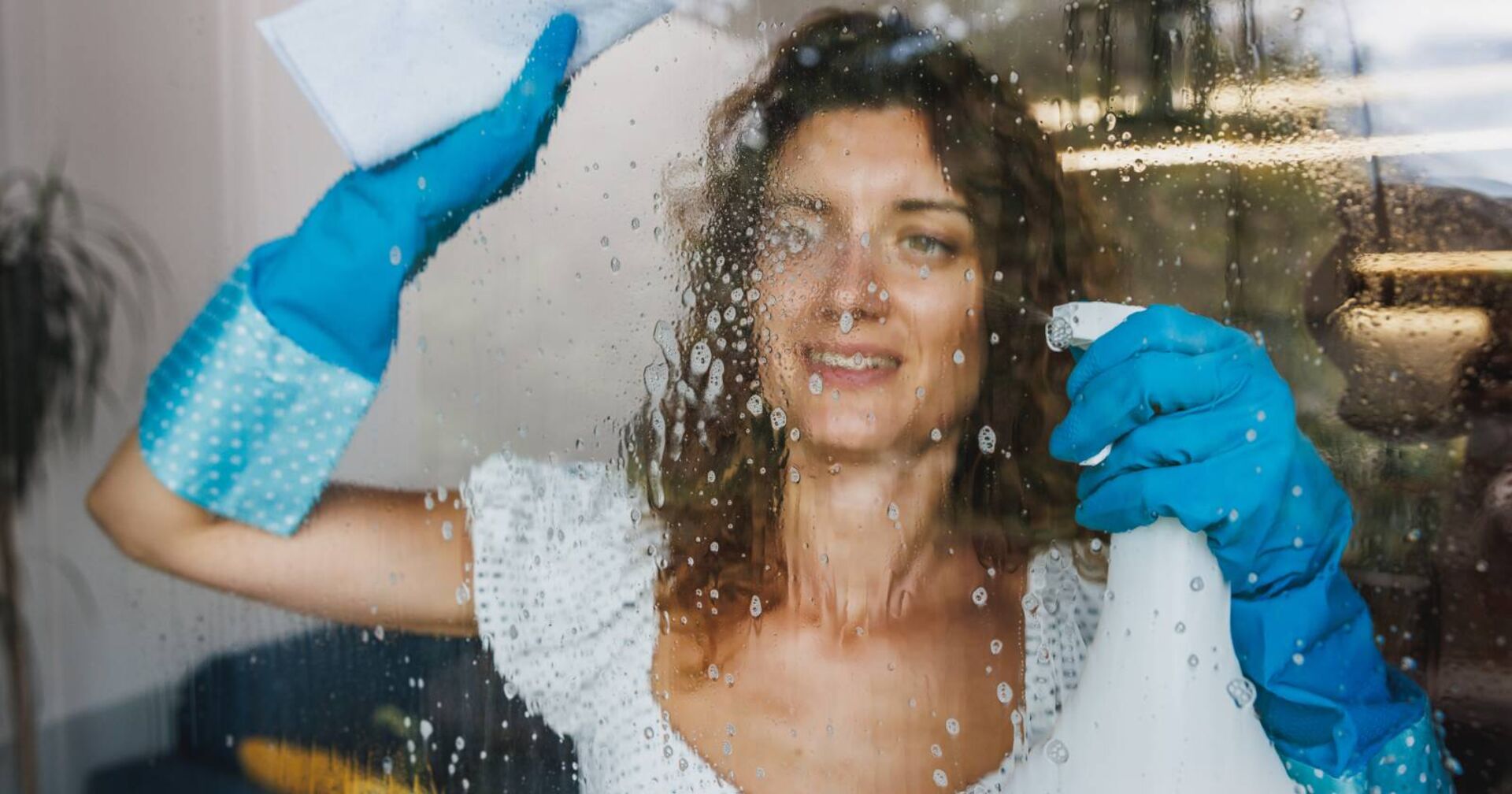 Frau beim Besprühen von Fenstern mit einer Sprühflasche zum Reinigen von Fenstern