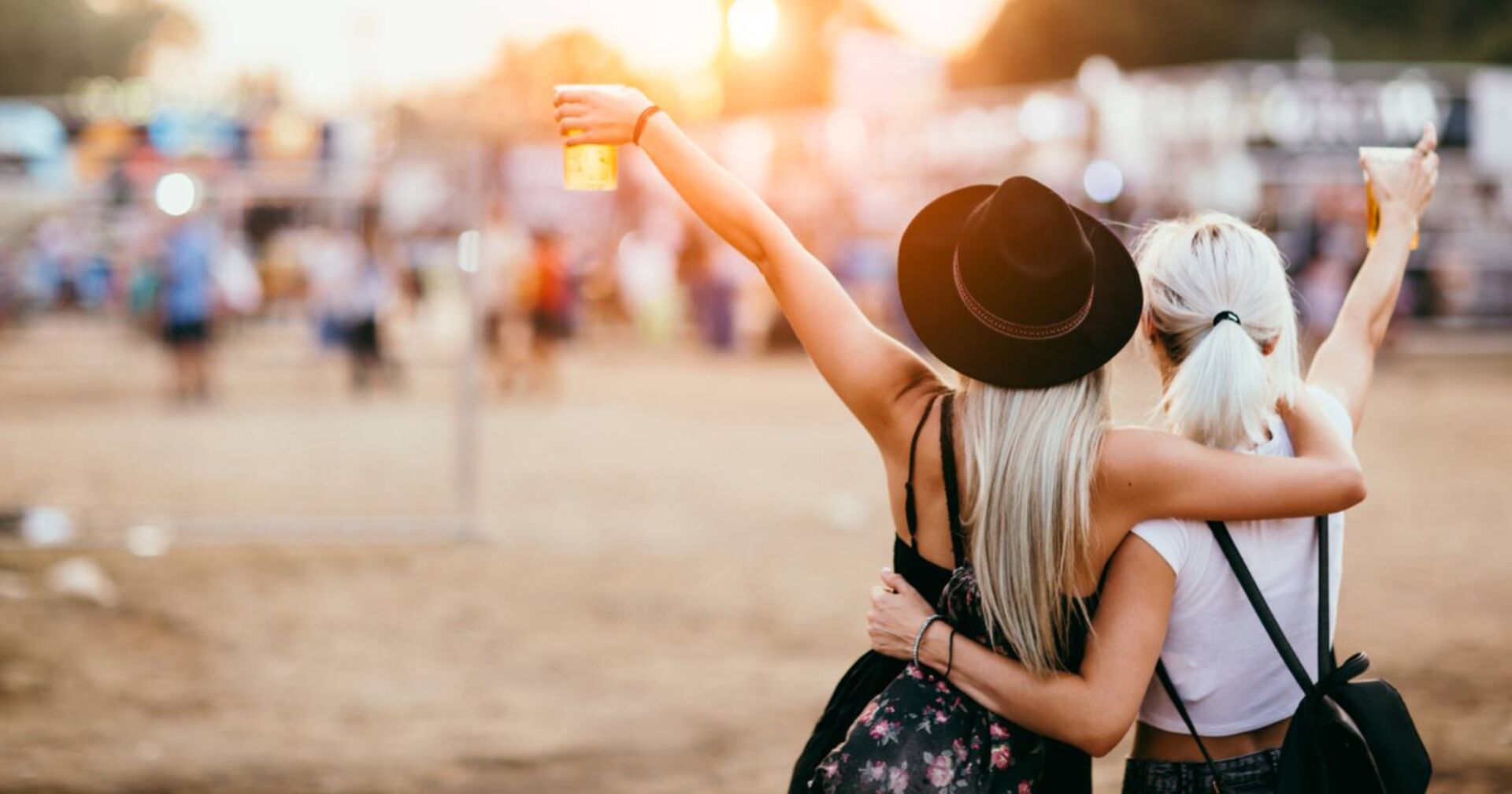 Zwei Freundinnen, die bei einem Musikfestival eng umschlungen bei einem Bier in der Hand ihre Lieblingskünstlerin anfeuern.
