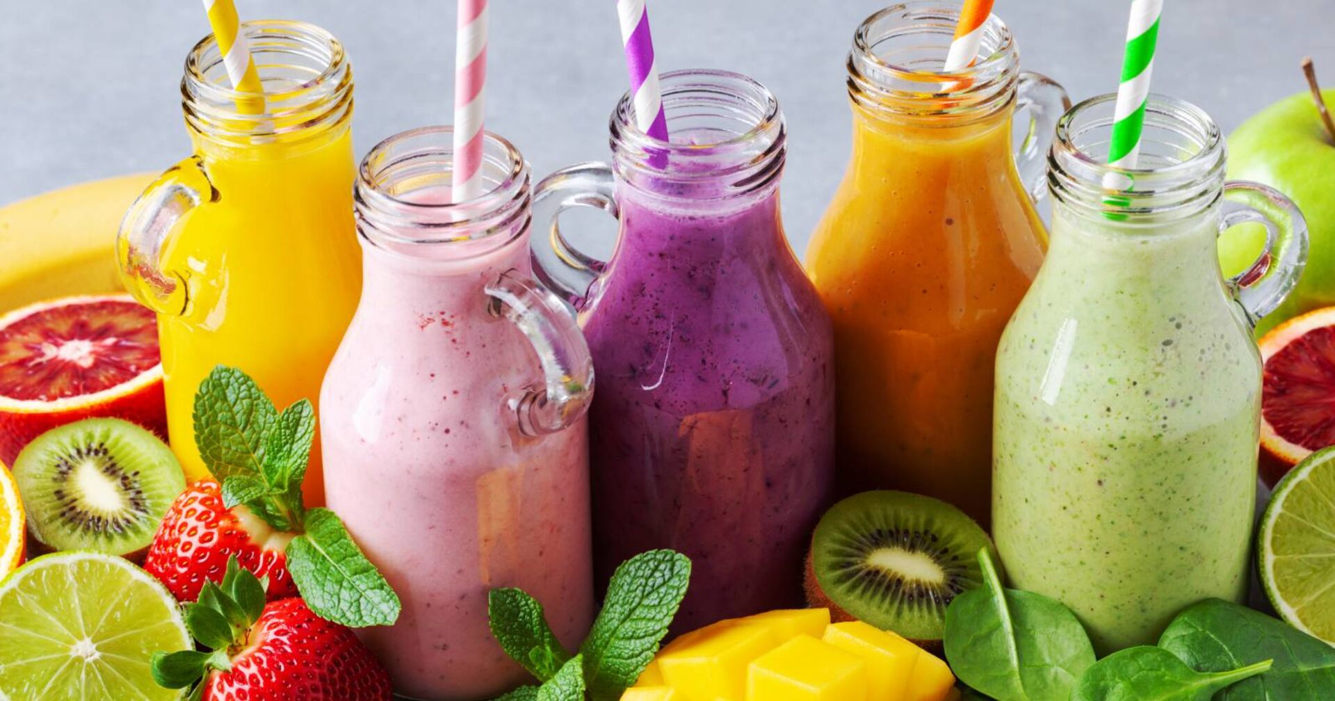 5 Glasflaschen mit bunten Smoothies aus frischem Obst und Gemüse.