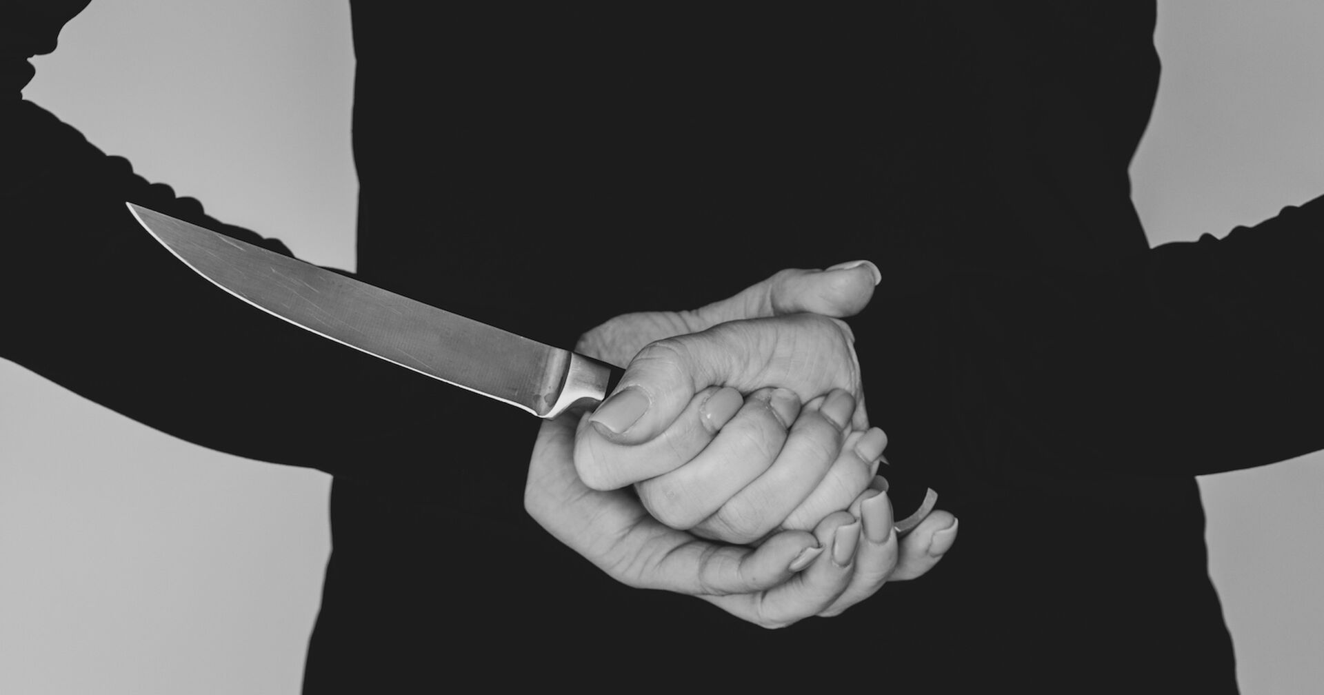 Eine Frau versteckt ein Messer hinter dem Rücken.