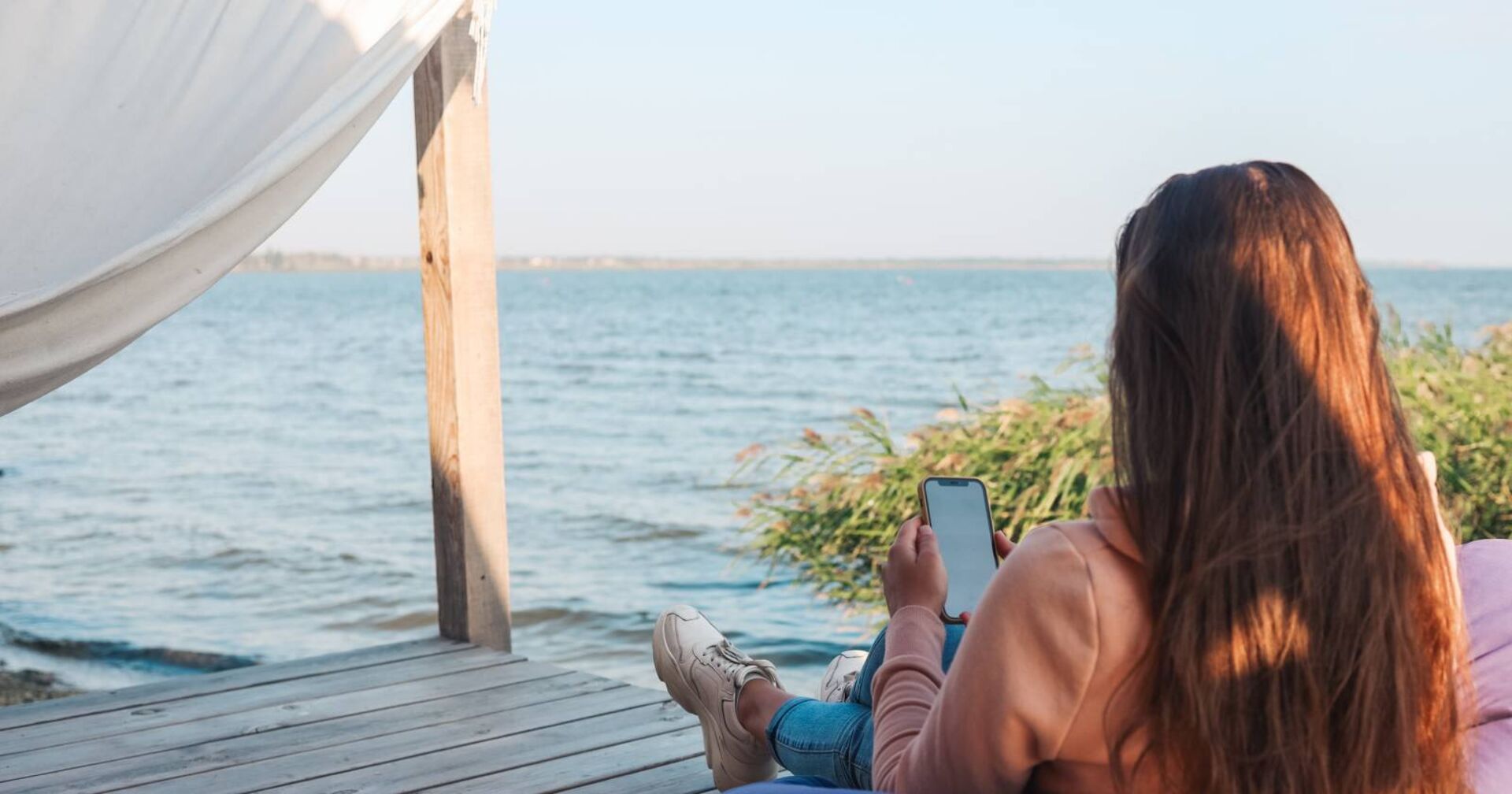 Frau entspannt mit dem Rücken zum Betrachter bei Sonnenuntergang am Seeufer