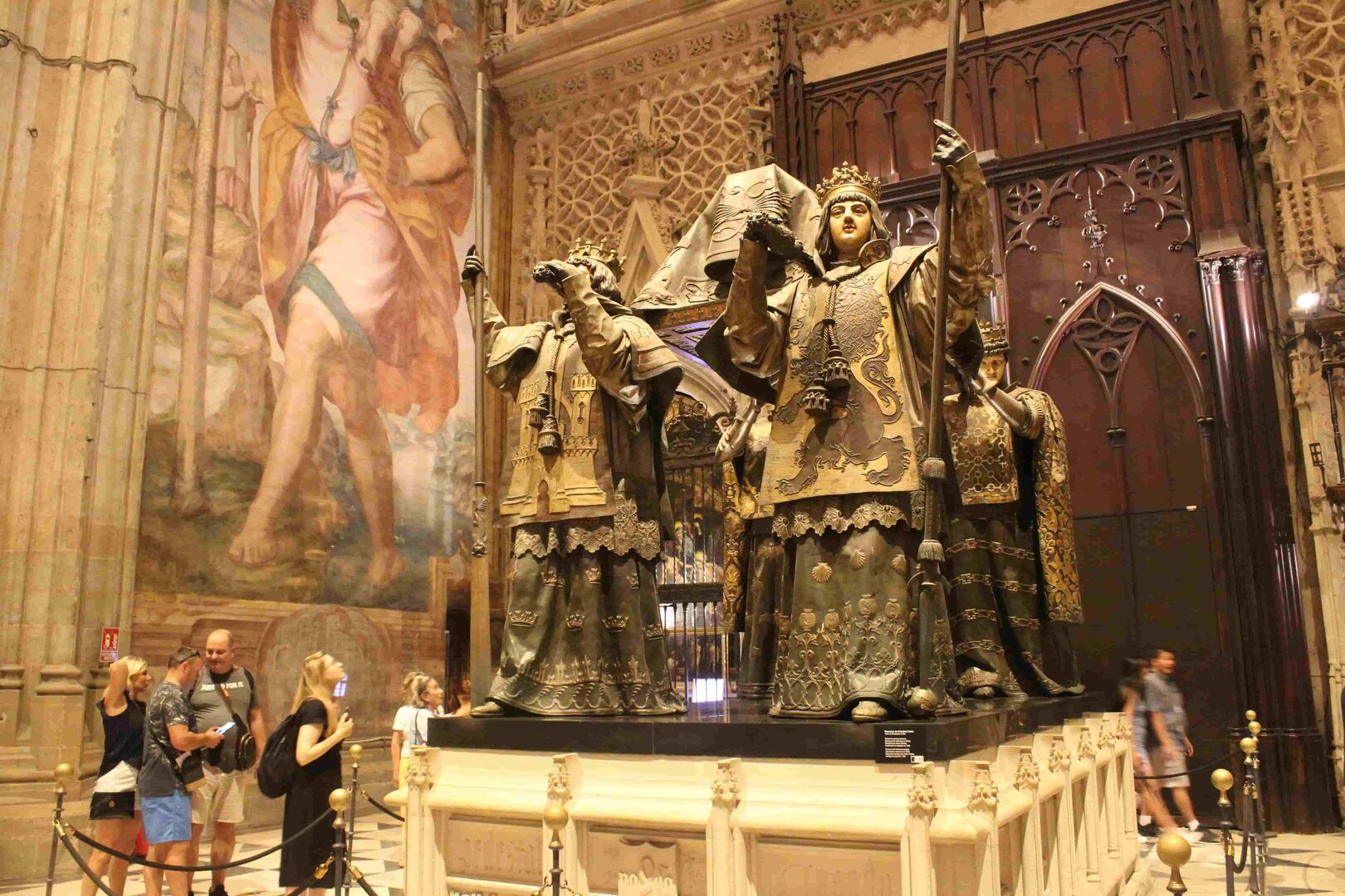 Das Grab von Christoph Kolumbus  in der Kathedrale von Sevilla: Vier Herolde stemmen das reich verzierte Grab den Entdeckers. Links: Einige Touristen fotografieren das in braunen Farben gehalten Monument.
