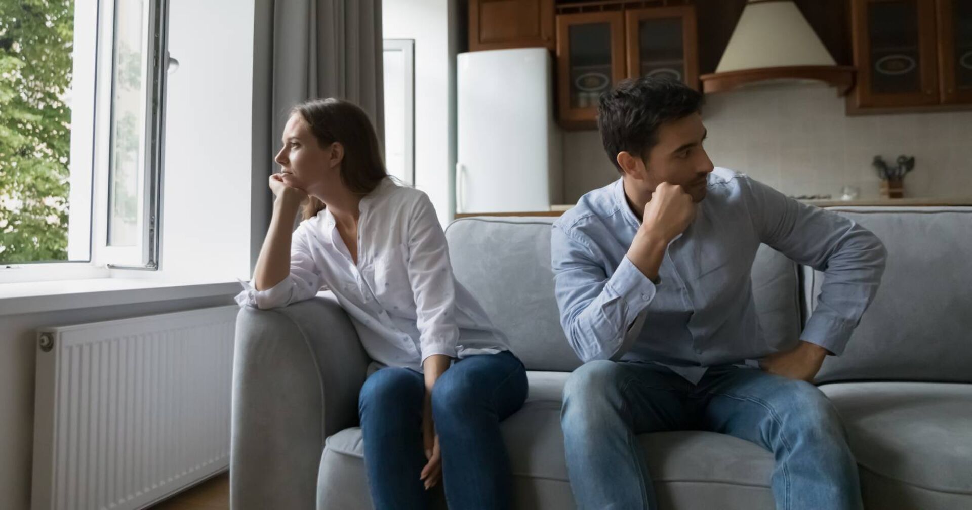Paar, das zusammen auf einem Sofa sitzt, aber in entgegengesetzte Richtungen blickt.