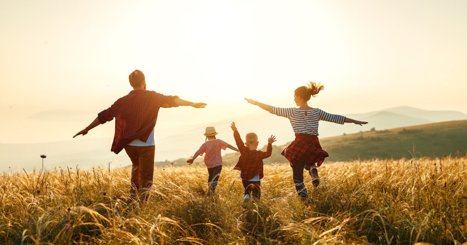 Ein Pärchen läuft mit seinen beiden Kindern über eine Wiese dem schönen Sonnenschein entgegen | Credit: iStock.com/evgenyatamanenko