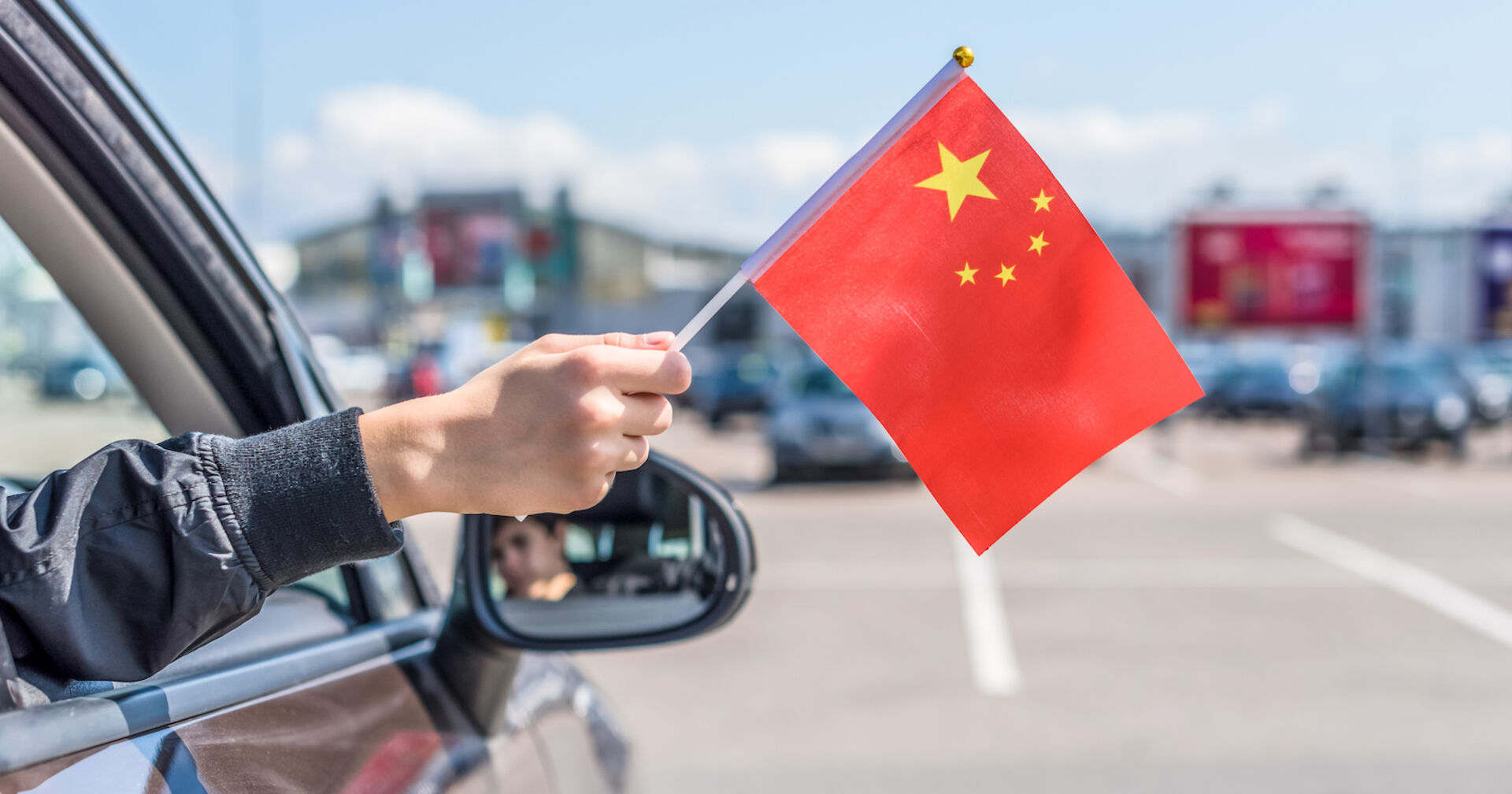 Hand hält chinesische Fahne aus dem Autofenster