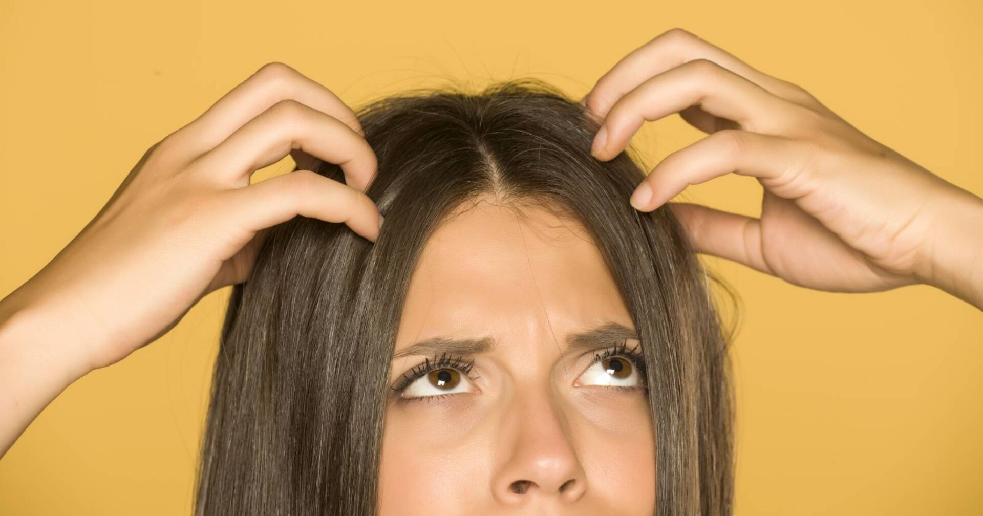 Frau greift sich an den Kopf und kratzt sich an der Kopfhaut