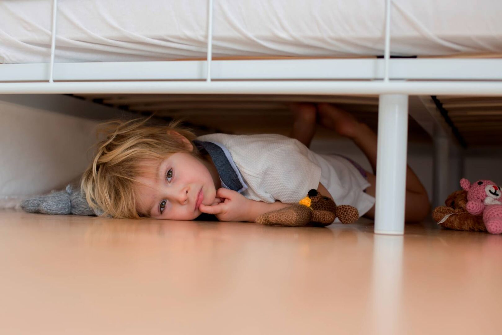 Kleiner Junge liegt ängstlich unter dem Bett weil er nicht schlafen gehen möchte.