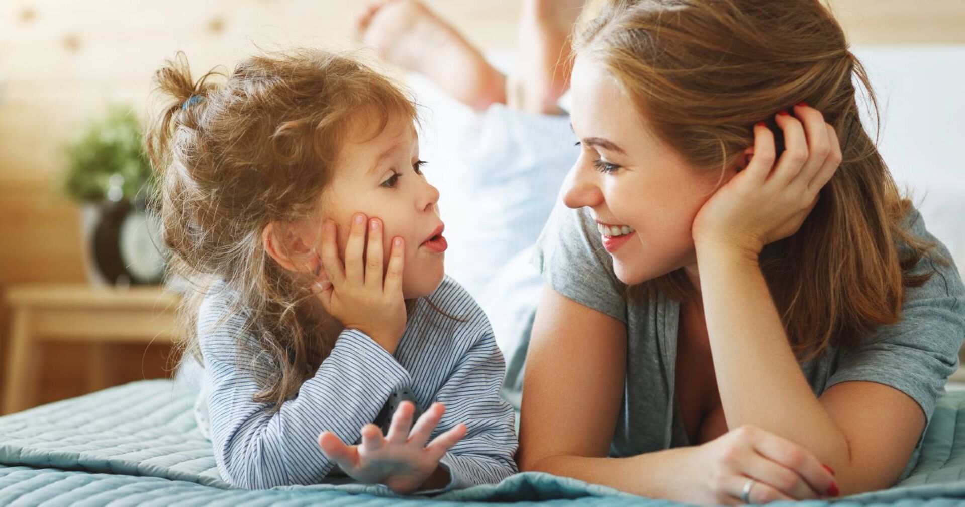 Kleinkind und ältere Schwester liegen gemeinsam auf dem Bett, dabei haben sie die Hände an den Kopf gestützt