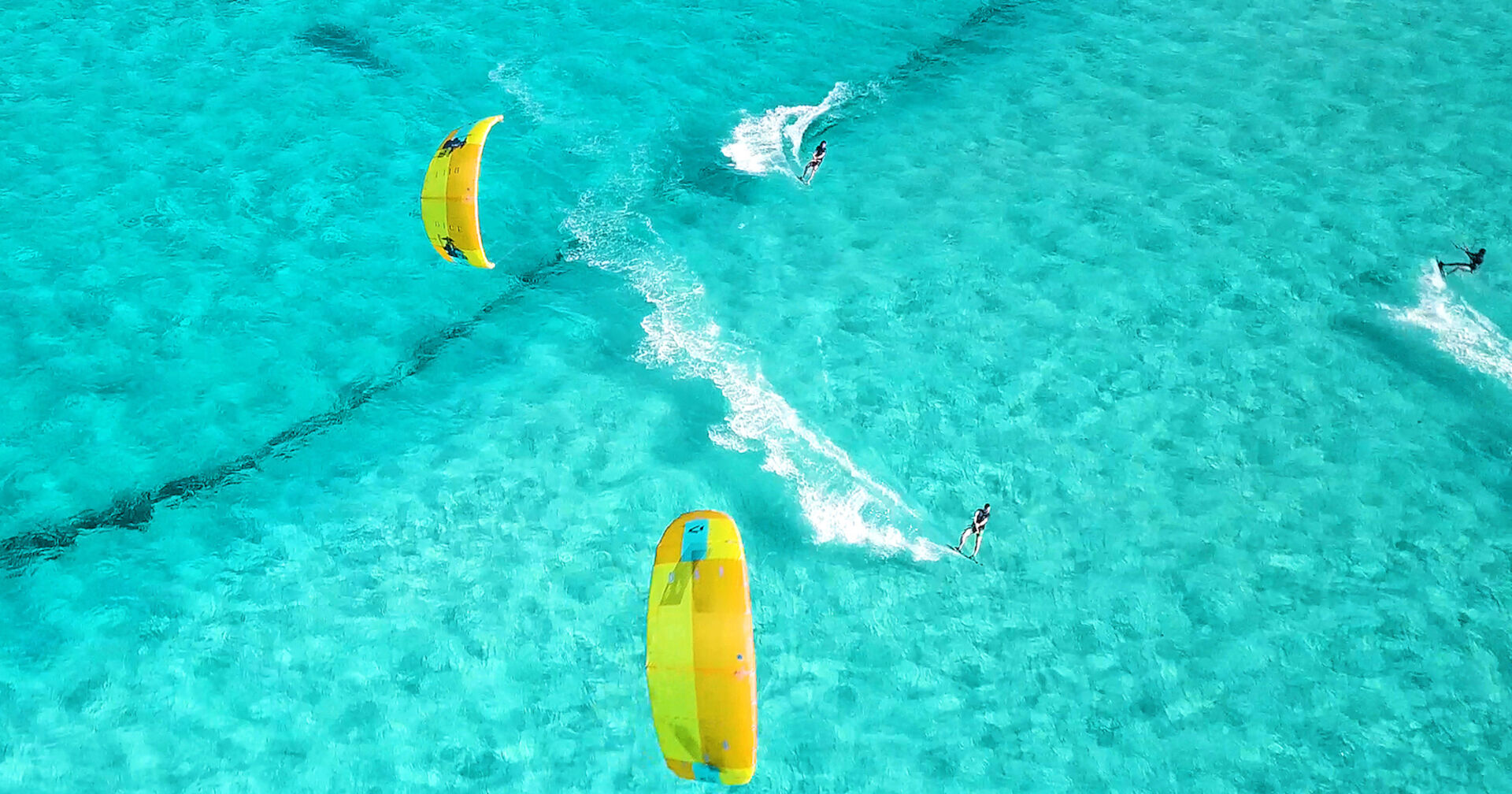 Drei Kitsurfer im türkis-blauen Meer