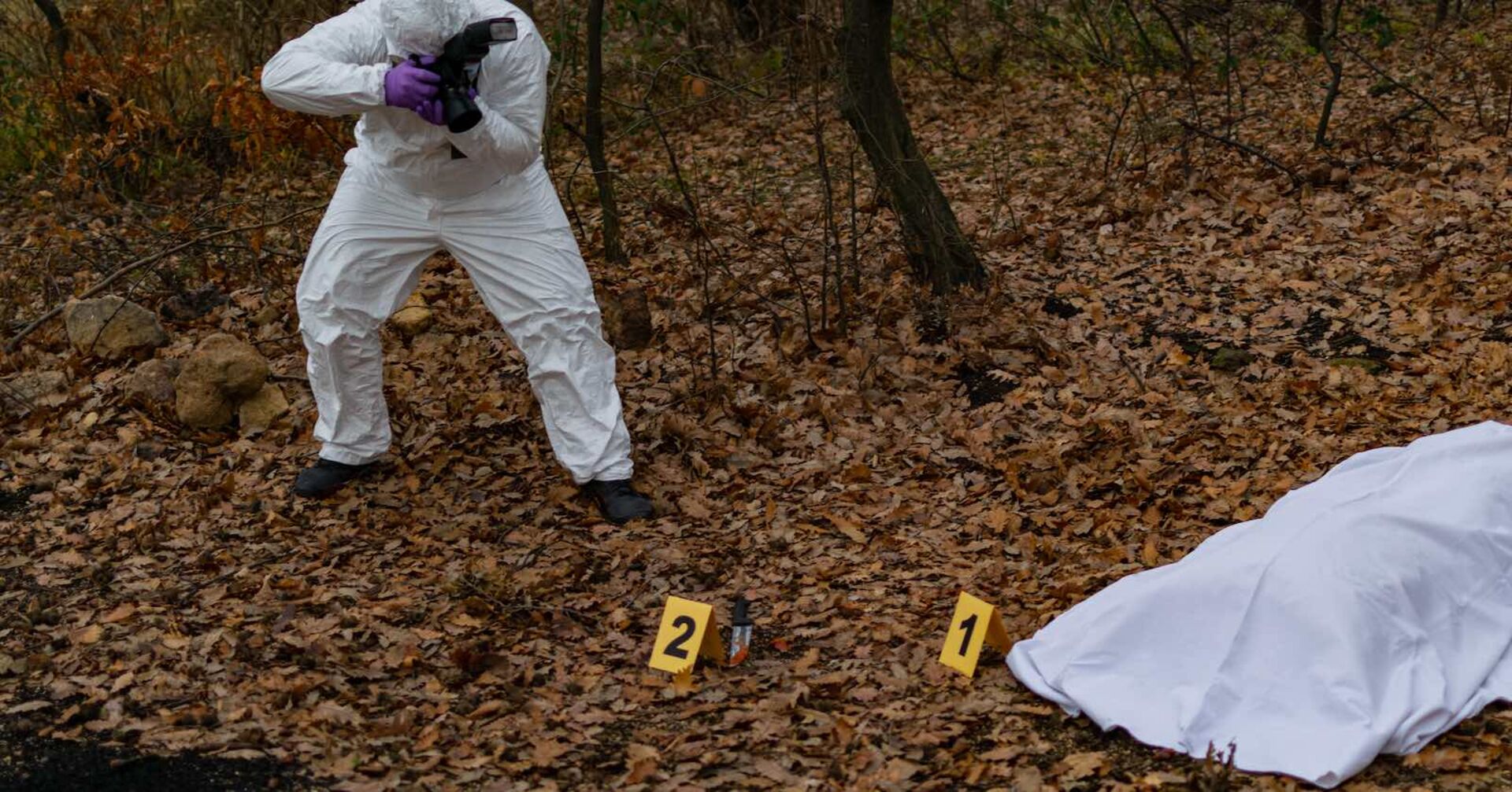 Ein Forensiker fotografiert eine abgedeckte Leiche.