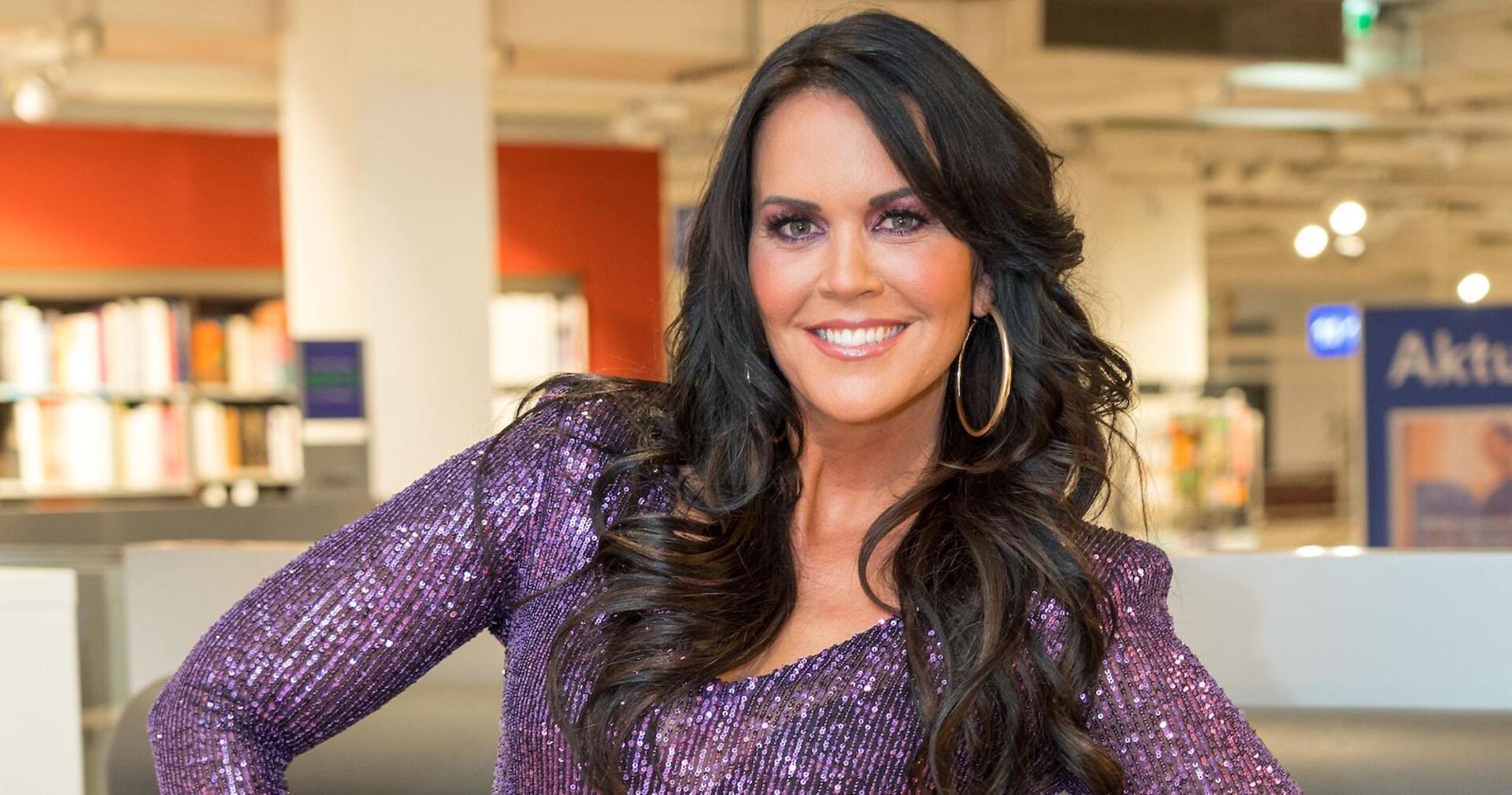 Martina Reuter in einem violett glitzer Outfit mit offenen schwarzen Haaren.