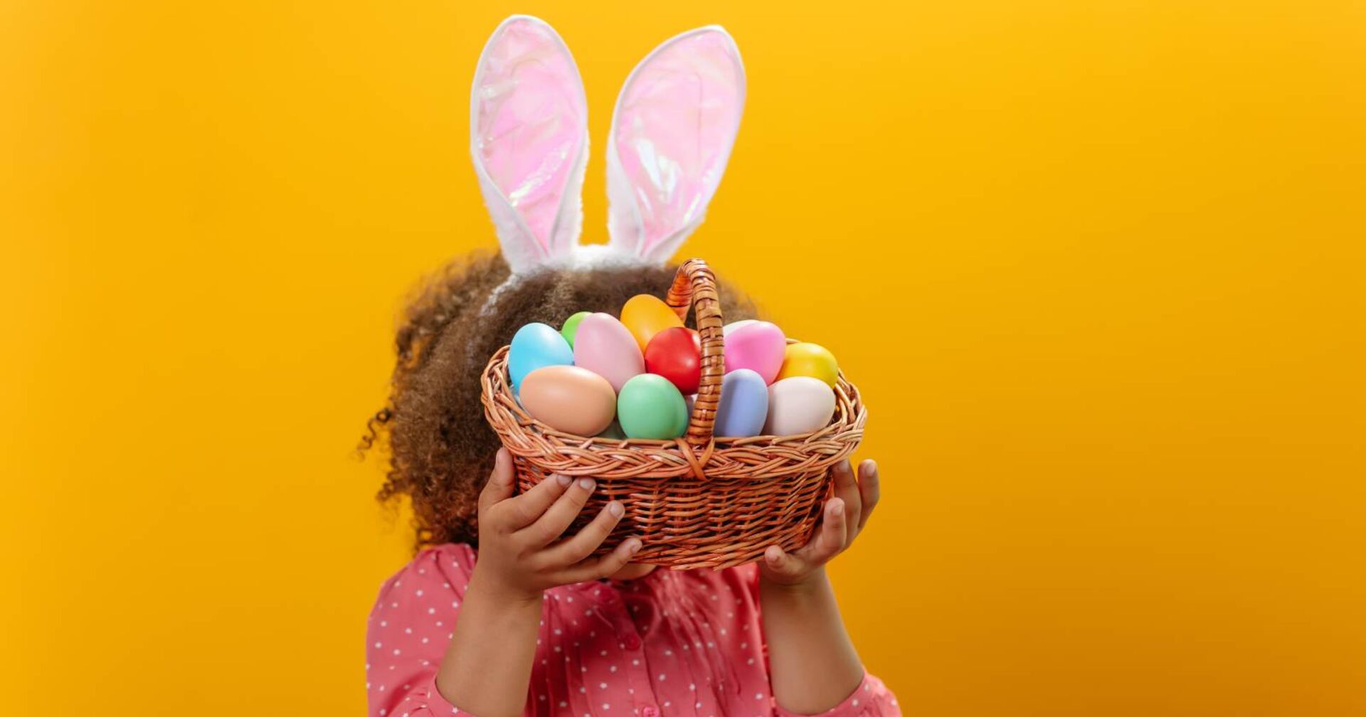 Mädchen mit Hasenohrenhaarreif und Osterkörbchen in den Händen, das ihr Gesicht teilweise verdeckt