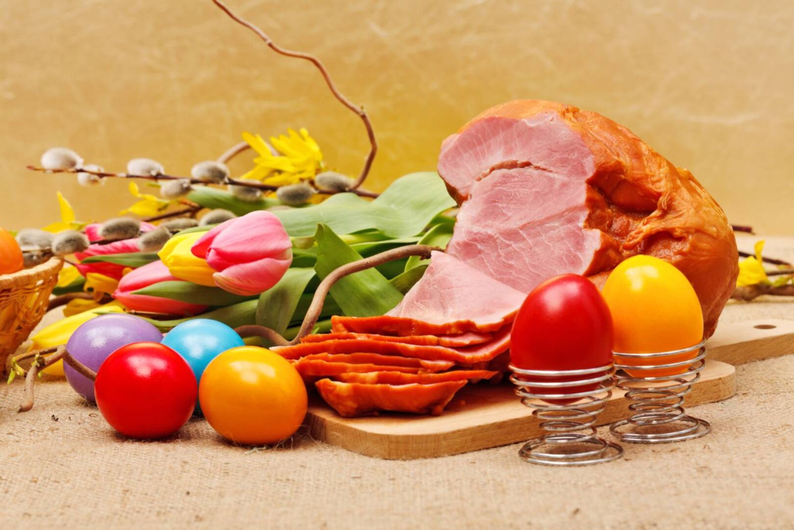 Aufgeschnittener, ganzer Schinken auf einem Holzbrett, dekoriert mit frisch gefärbten Ostereiern