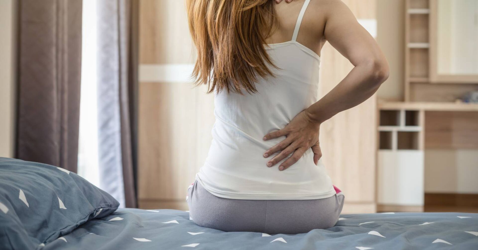 Frau auf dem Bett sitzend, den Rücken abstützend