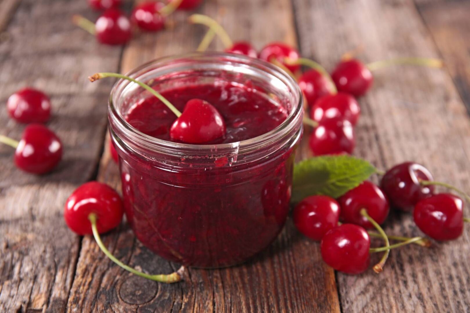 Marmeladenglas gefüllt mit Kirschmarmelade, zusätzlich gefüllt mit roten Kirschen