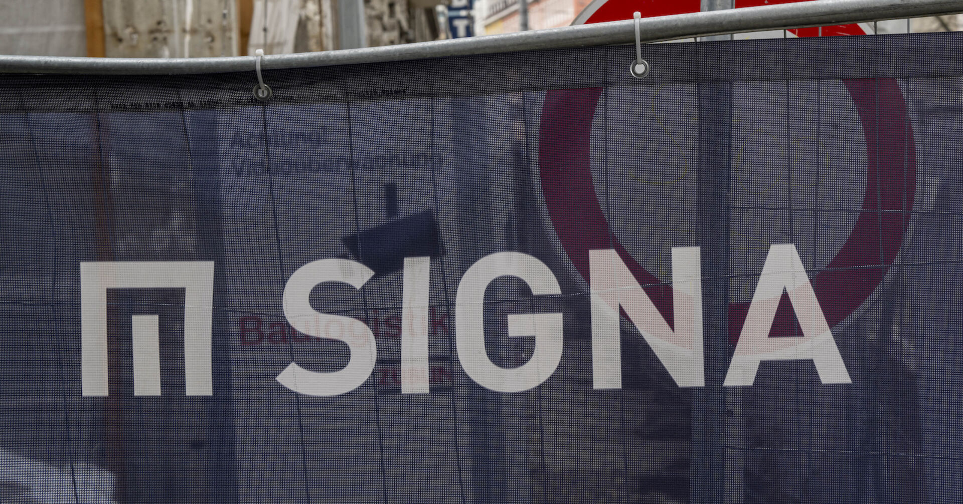 Eine Bauplane mit Logo und Schriftzug der Signa, dahinter ein Stoppschild