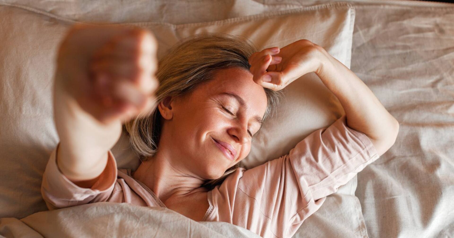 Eine Frau mittleren Alters, die sich nach einem erholsamen Schlaf genüsslich im Bett streckt
