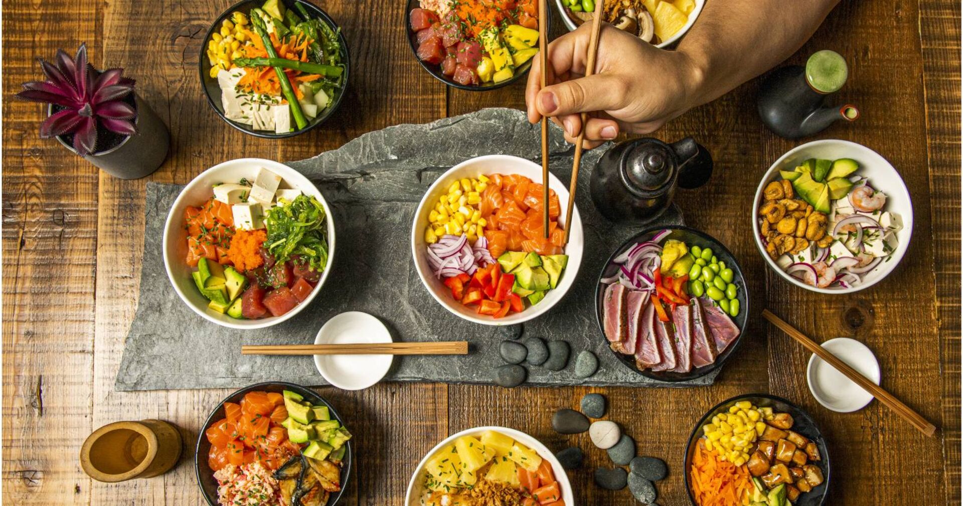 Vogelperspektive auf einen Tisch mit 7 verschiedenen Sushi Bowls.