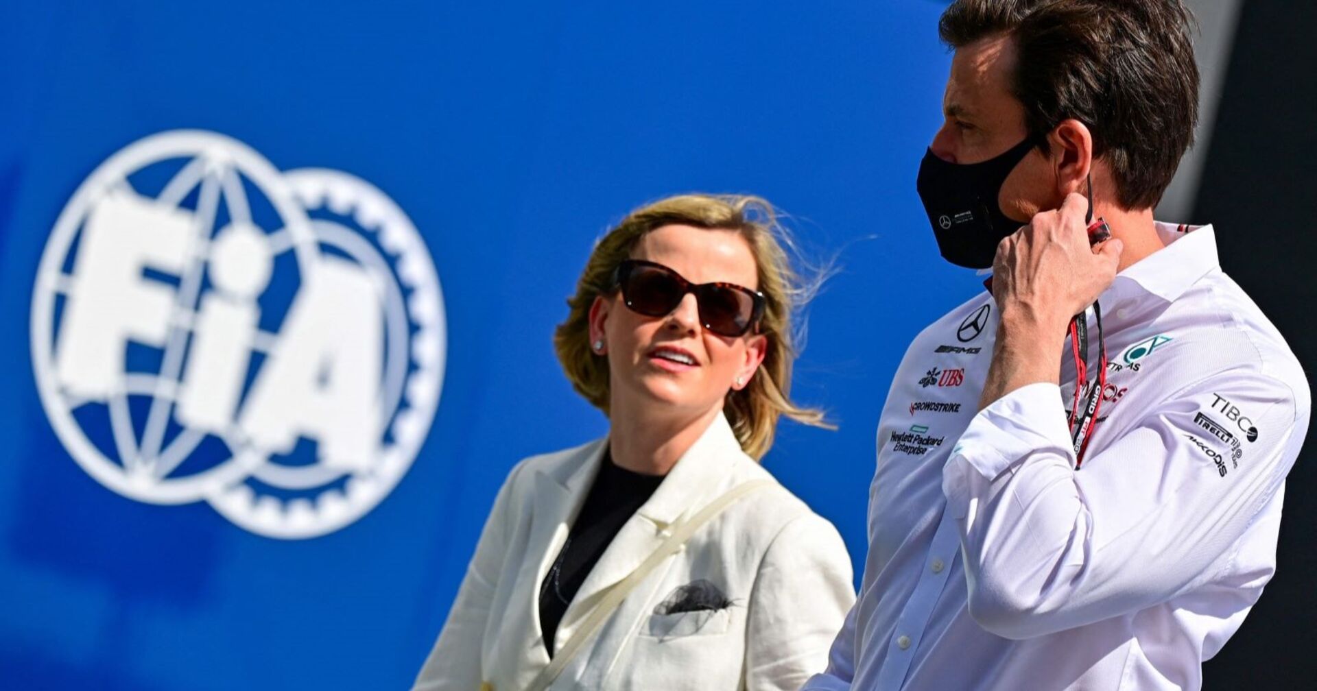 Susie und Toto Wolff vor dem Logo der FIA. Toto Wolff trägt eine Maske