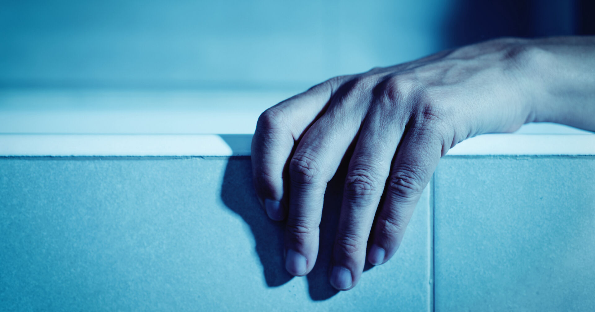 Eine Hand hängt über den Rand einer Badewanne.