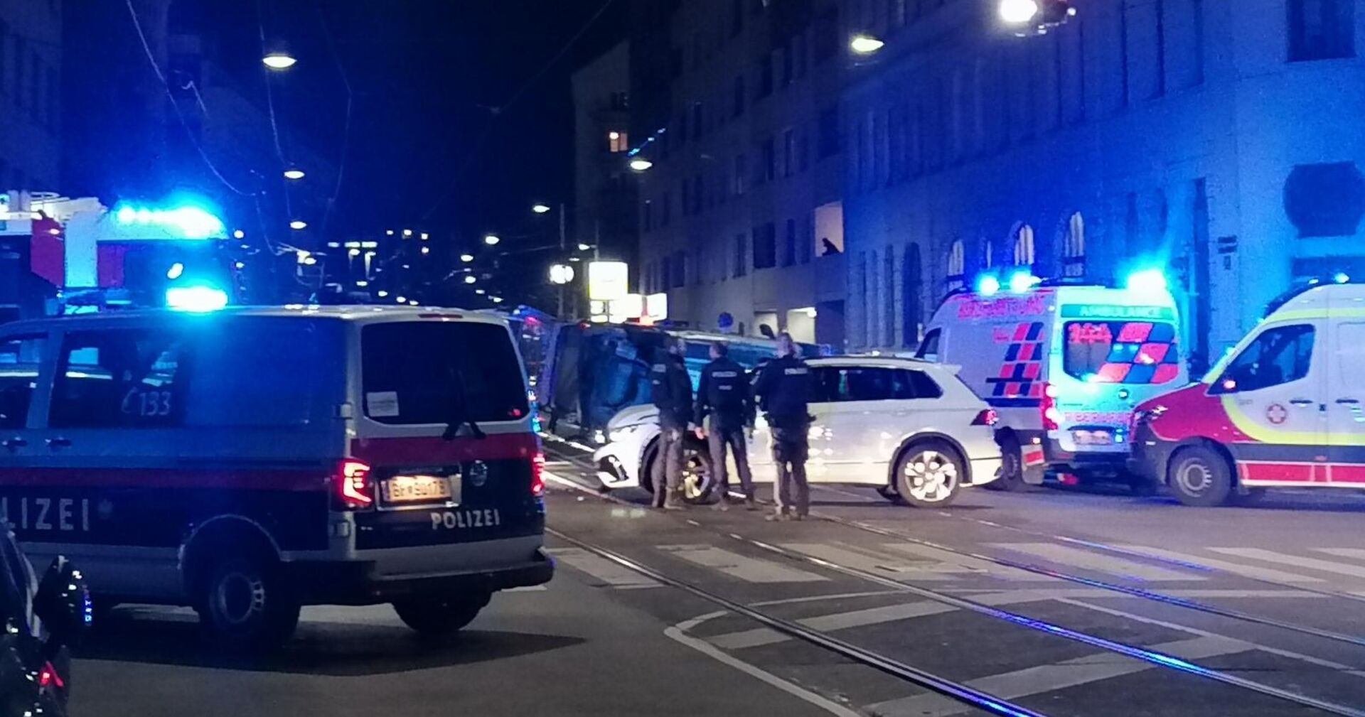 Polizei und Rettungswägen mit Blaulicht an einer nächtlichen Kreuzung. Beamte schirmen ein Fahrzueug ab, das sich überschlagen hat