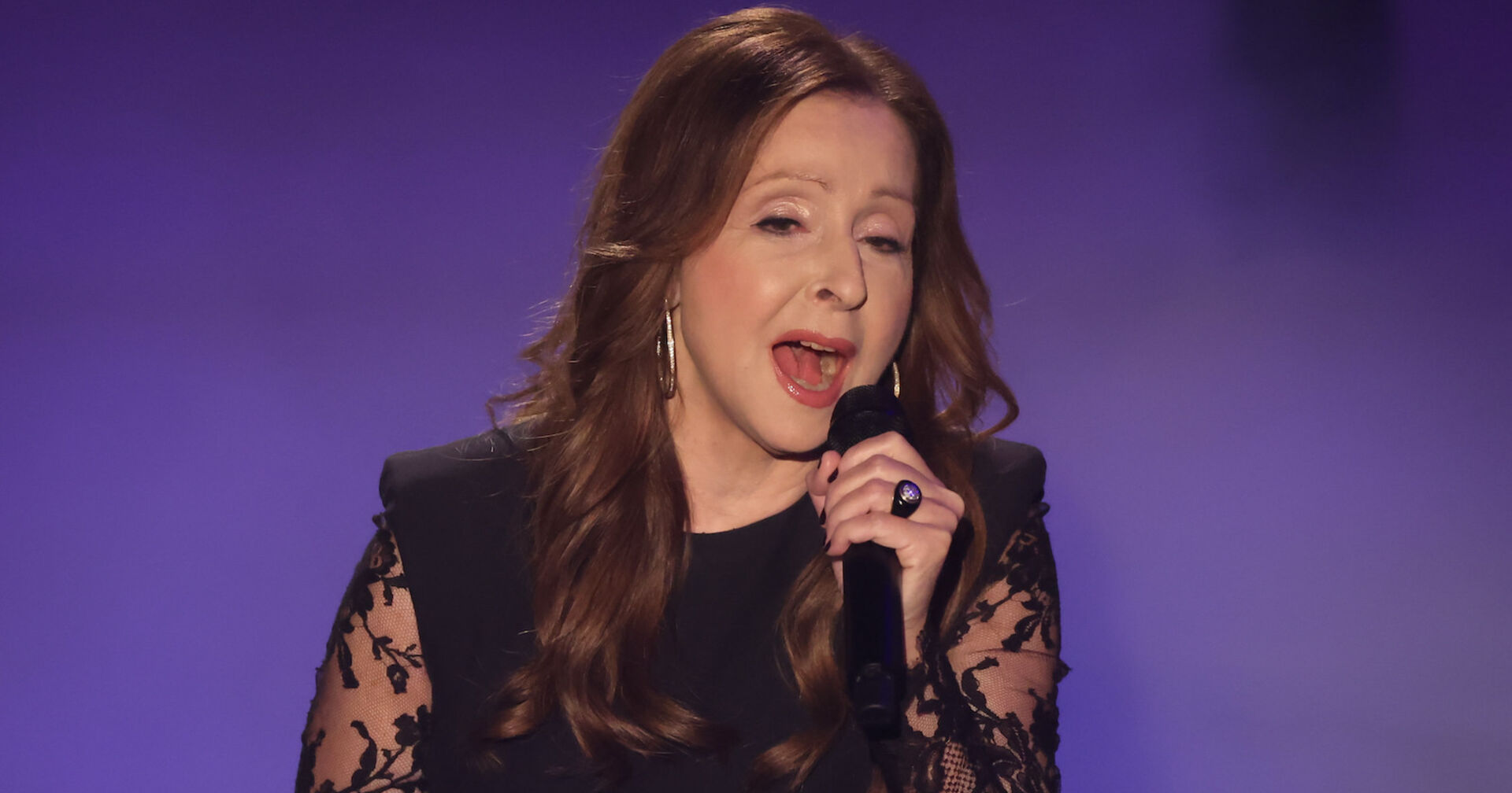 Vicky Leandros mit einem Mikrofon und einem Spitzenkleid auf der Bühne.