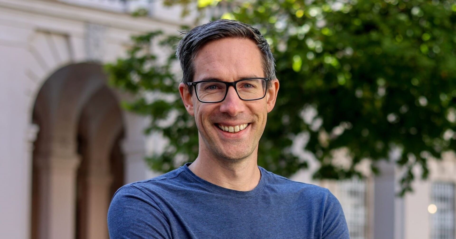 Kay-Michael Dankl im porträt. Er steht lachend im Freien und schaut direkt in die Kamera