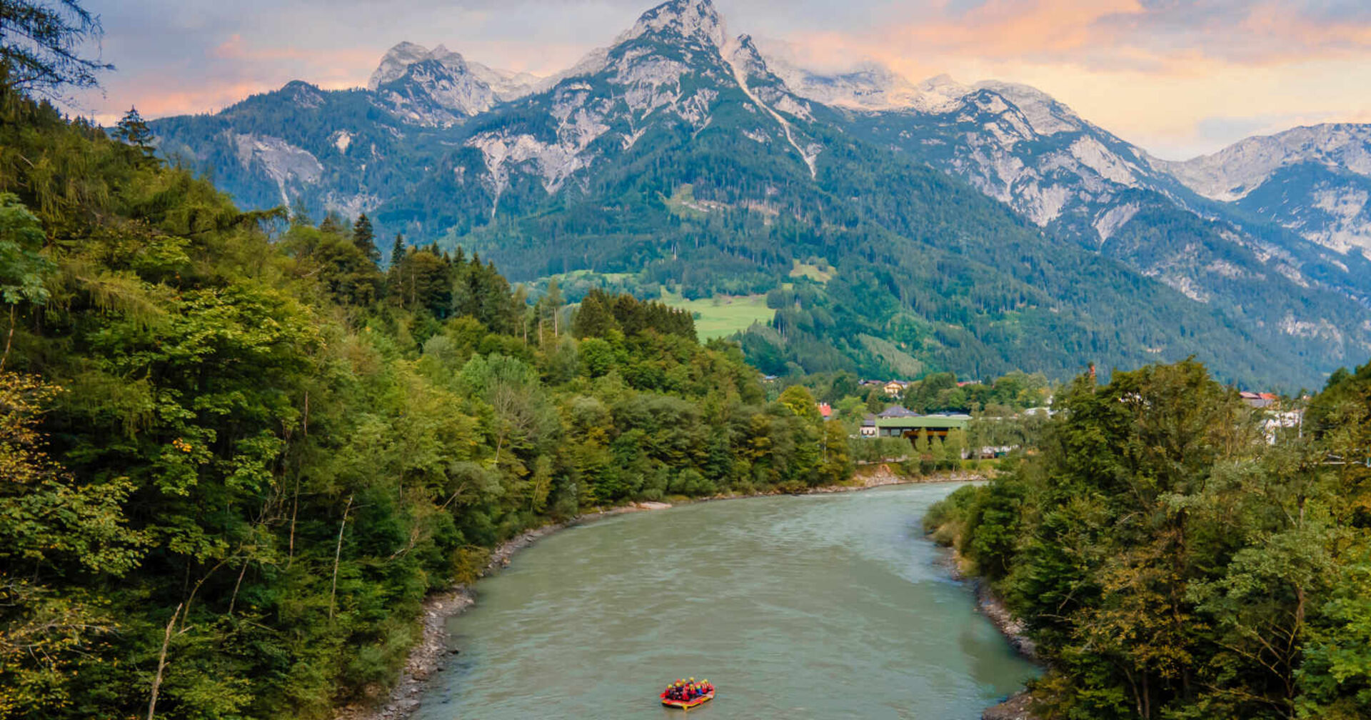 Eien Rafting-Gruppe auf einem Fluss, umgeben von Wald mit einem Blick auf österreichische Alpen.