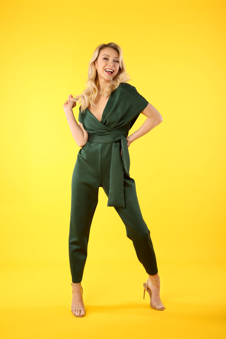 Blonde Frau in einem grünen Jumpsuit vor gelbem Hintergrund
