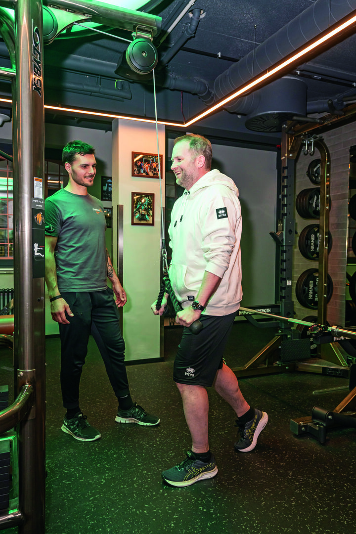 Mann trainiert gemeinsam mit einem Trainer im Fitnessstudio