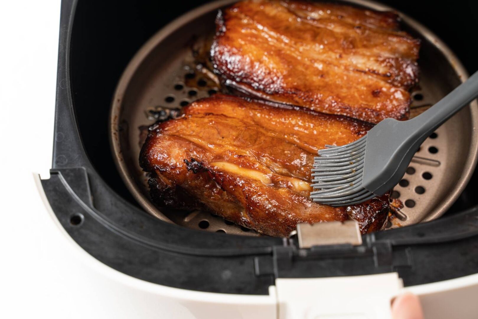 Schweinebauch im Airfryer, der gerade mit einer Marinade bepinselt wird