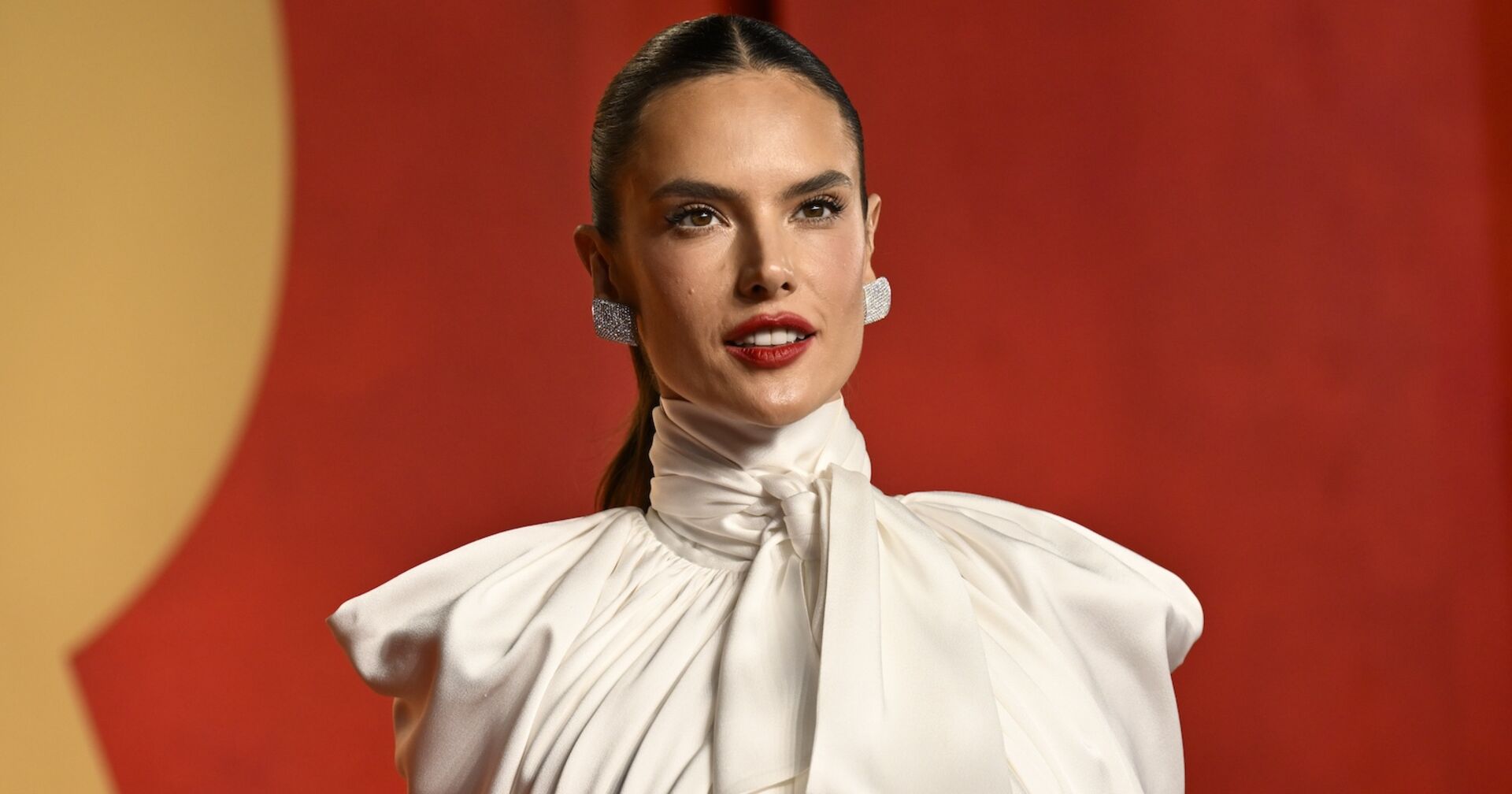 Alessandra Ambrosio mit einem weißen Oberteil und zurück gegelten Haaren auf dem Red Carpet.