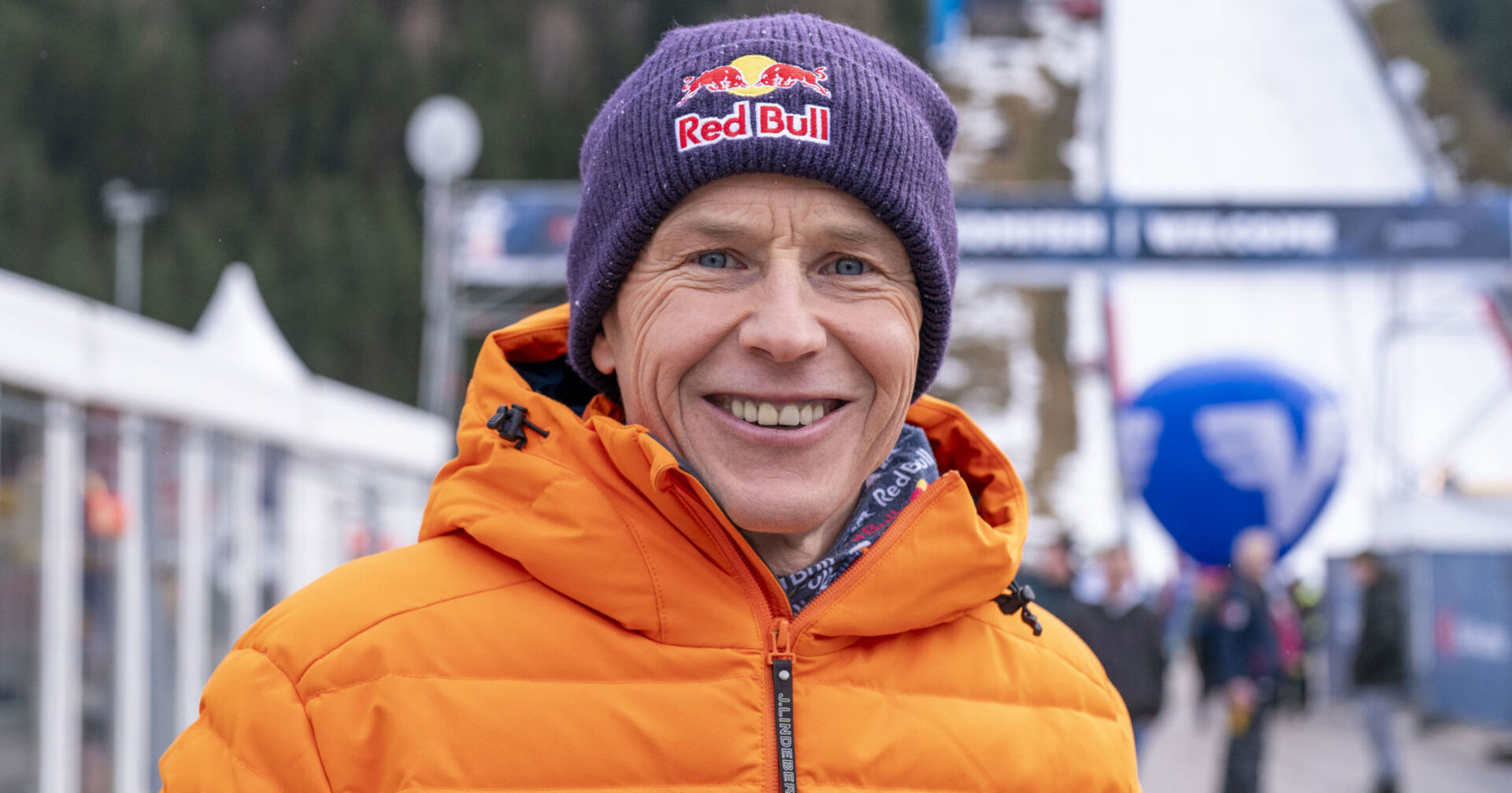 Ein Mann in oranger Skijacke und mit &quot;Red Bull&quot;-Haube steht vor einer Skipiste