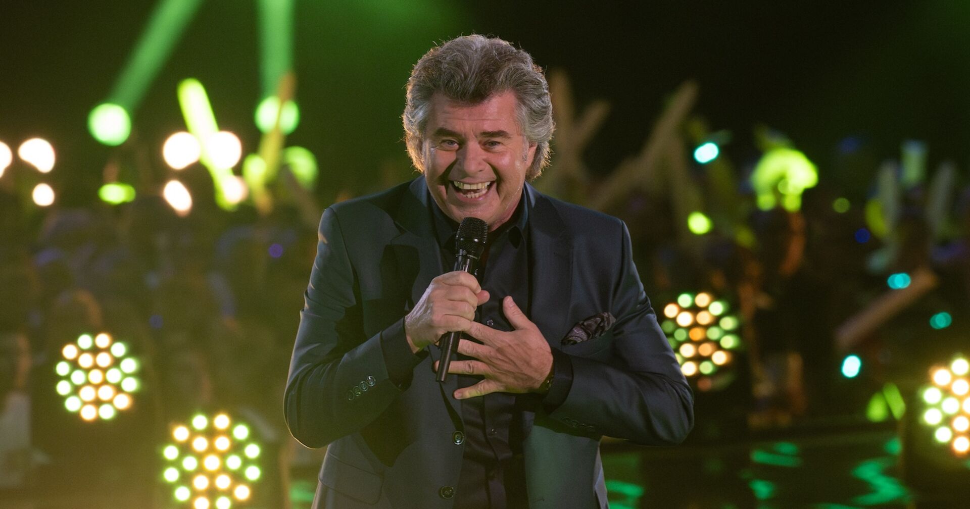 Andy Borg mit einem Mikrofon und einem schwarzen Sakko auf der Bühne.