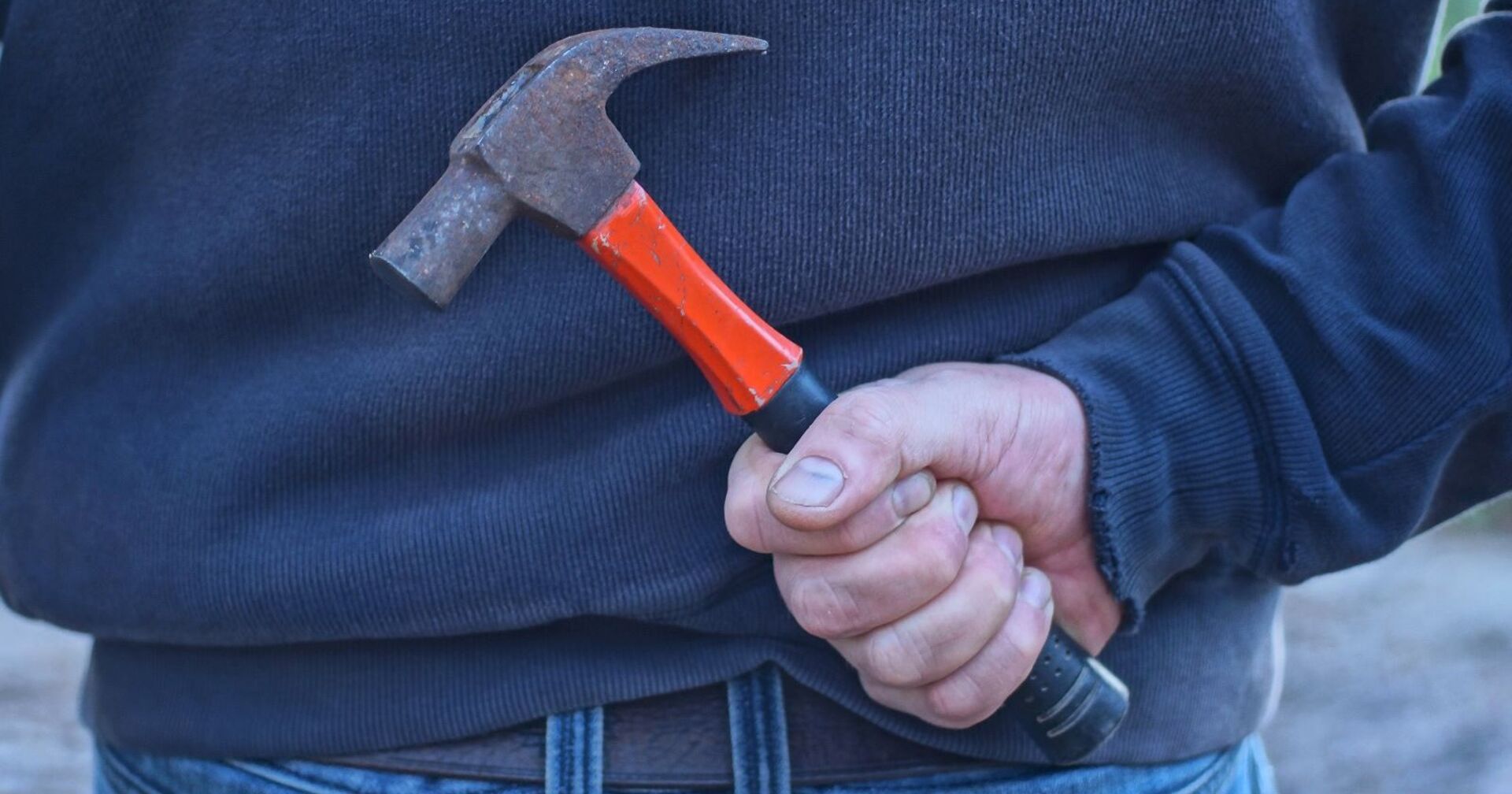 Ein Mann hält einen Hammer versteckt hinter seinem Rücken.
