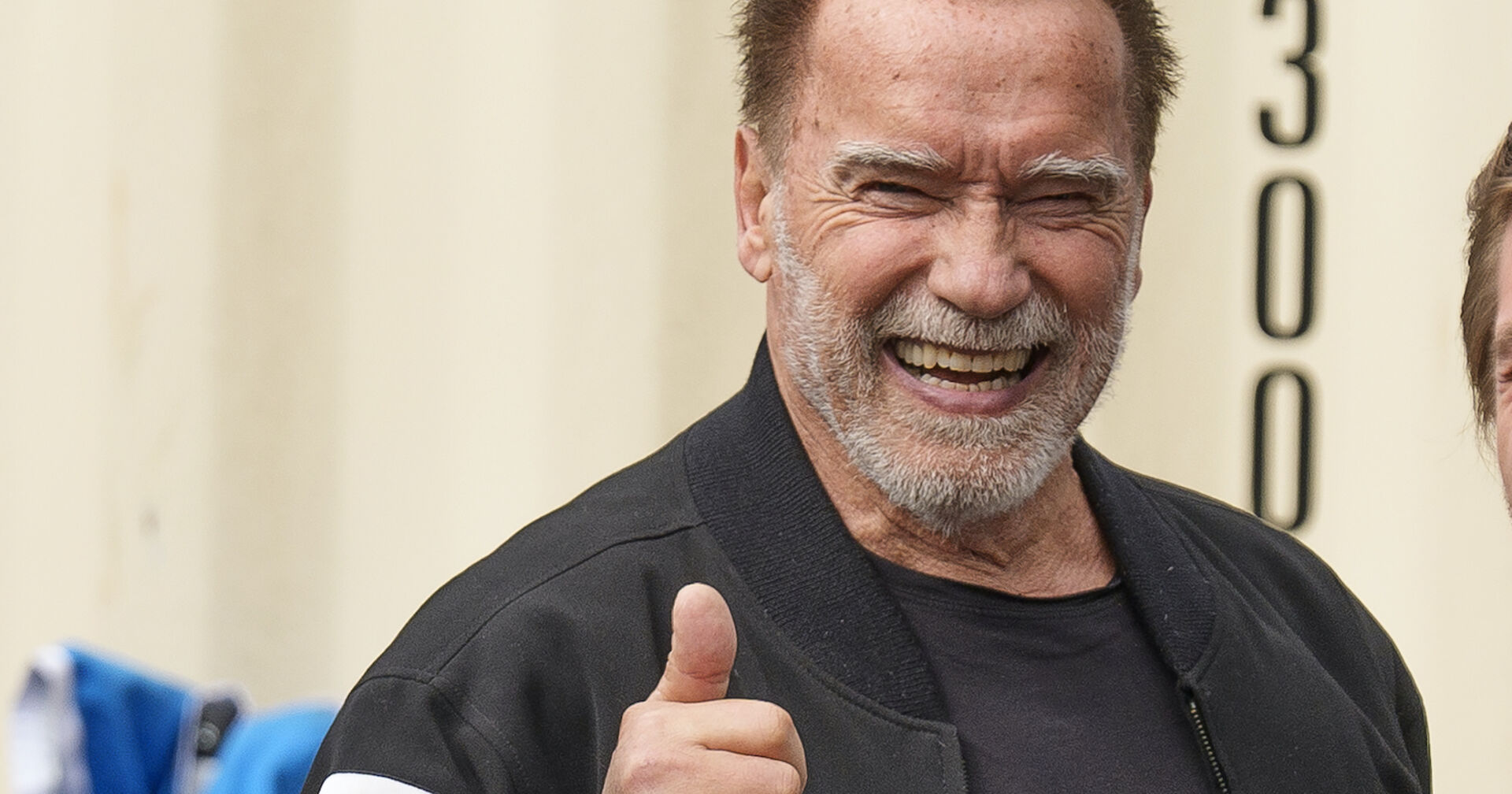 Arnold Schwarzenegger hält seinen Daumen hoch und lacht.